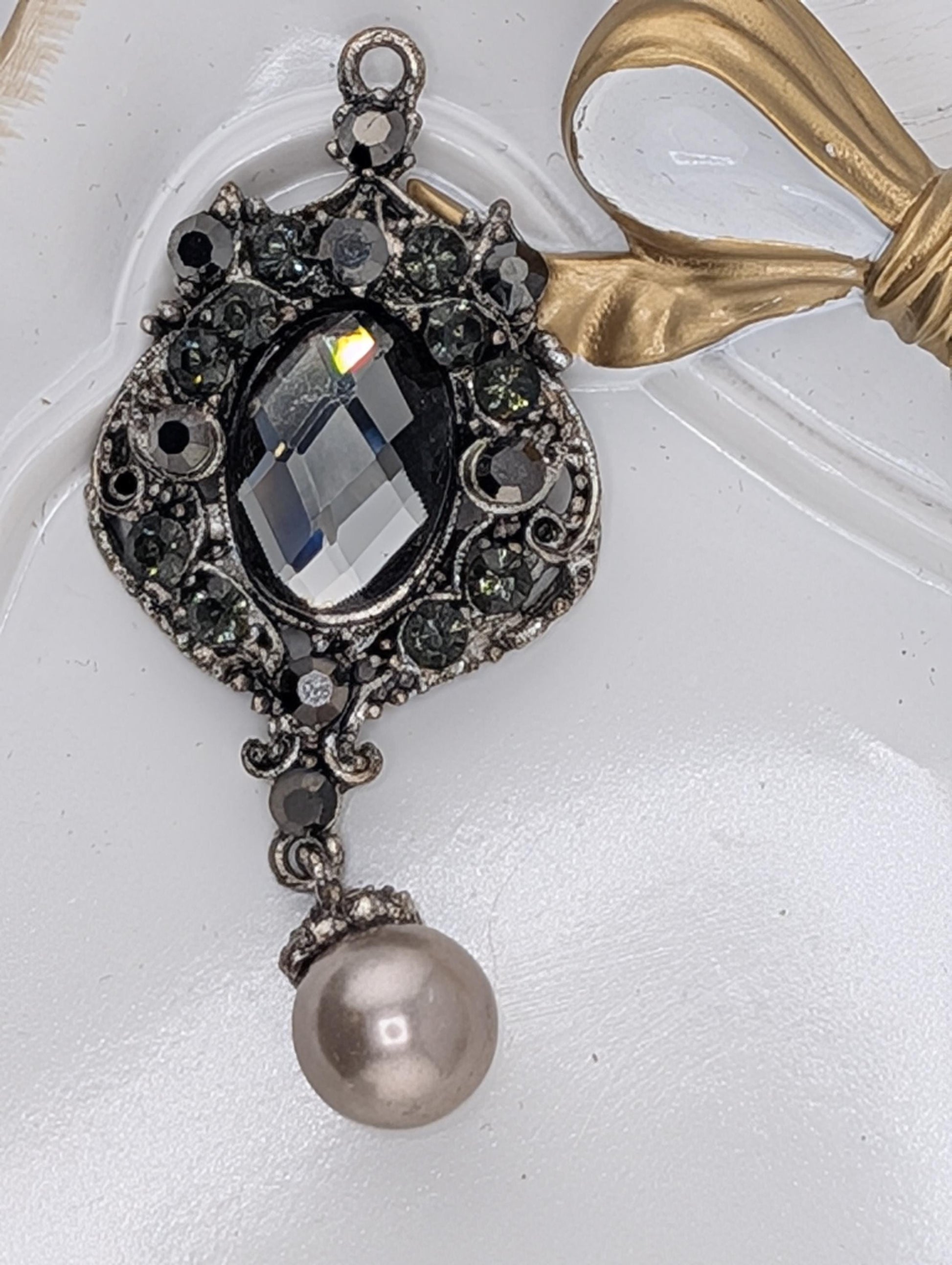 A decorative pendant with a large crystal stone, surrounded by smaller stones and pearls, and a gold ribbon.