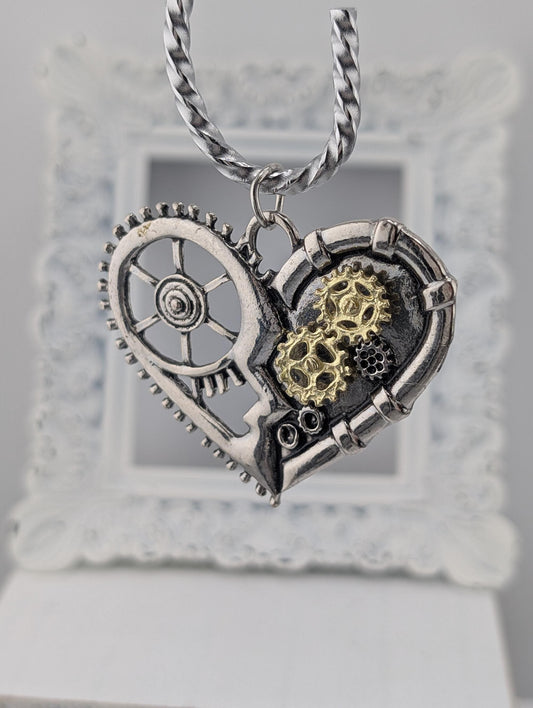 A silver heart-shaped pendant with gears and a wheel attached to it, hanging from a chain.