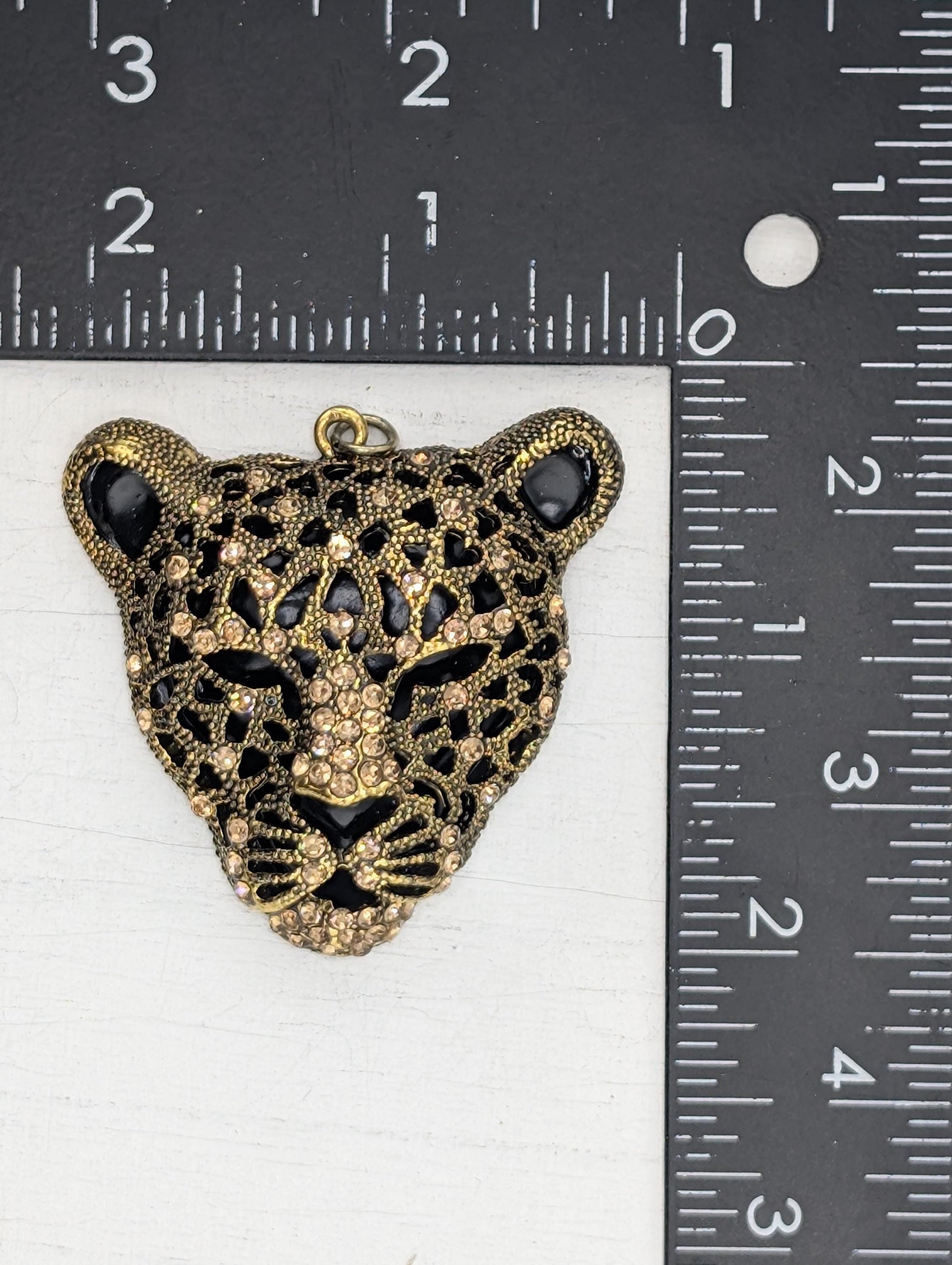 A close-up image of a decorative pendant in the shape of a leopard&#39;s head, adorned with rhinestones and gold accents.