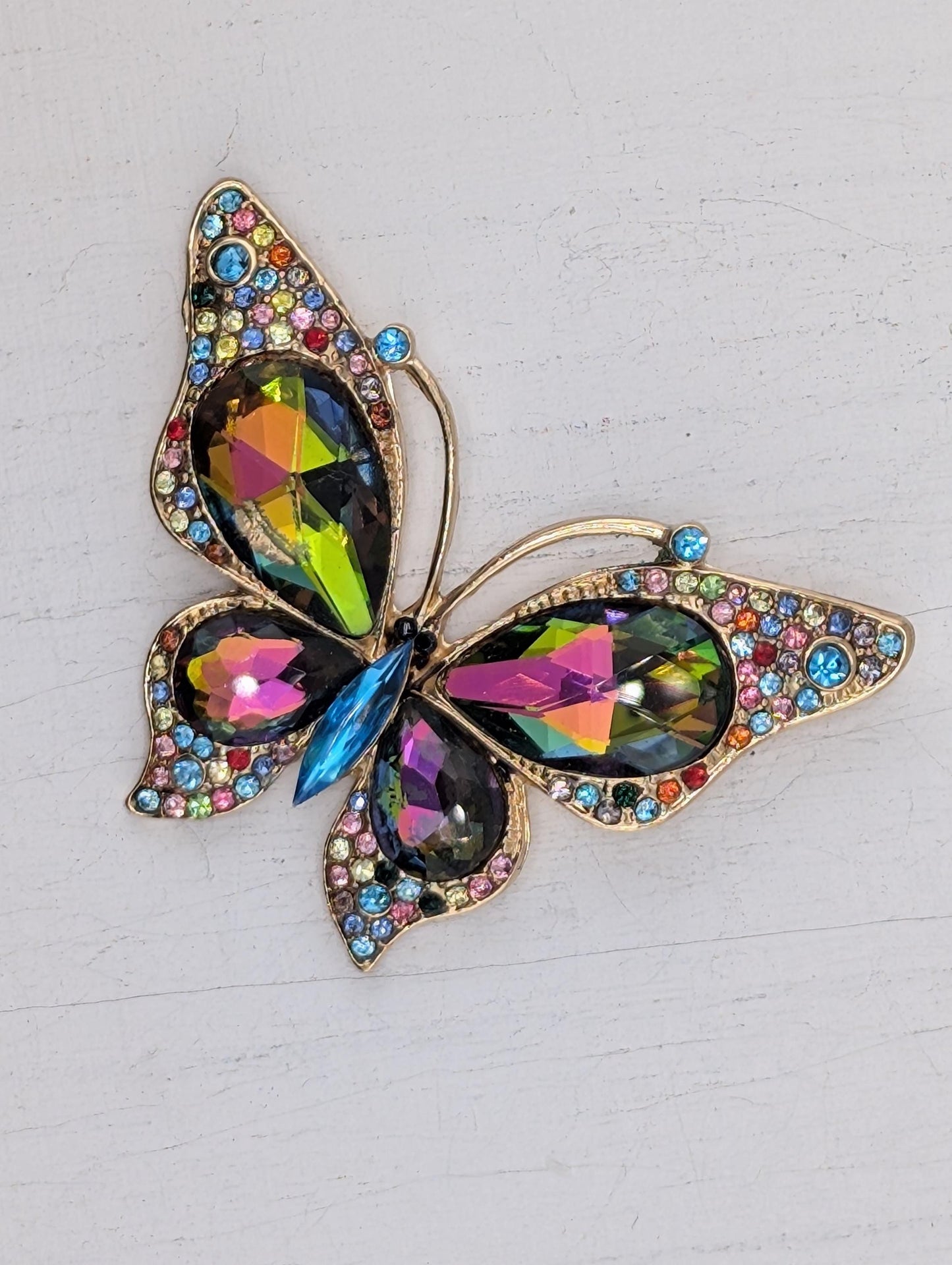A colorful butterfly brooch with a gold-colored frame and a variety of gemstones, including blue, green, pink, and yellow stones.