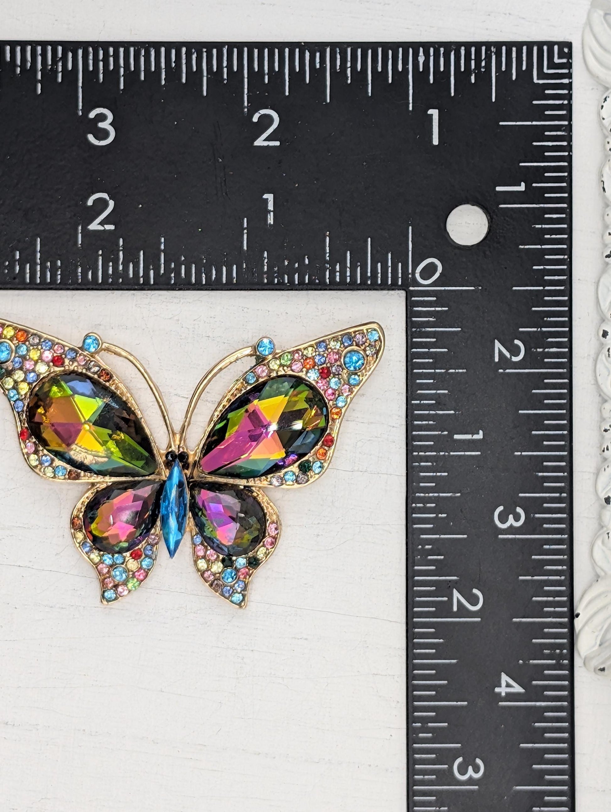 A colorful butterfly brooch with gemstones is being measured against a ruler.