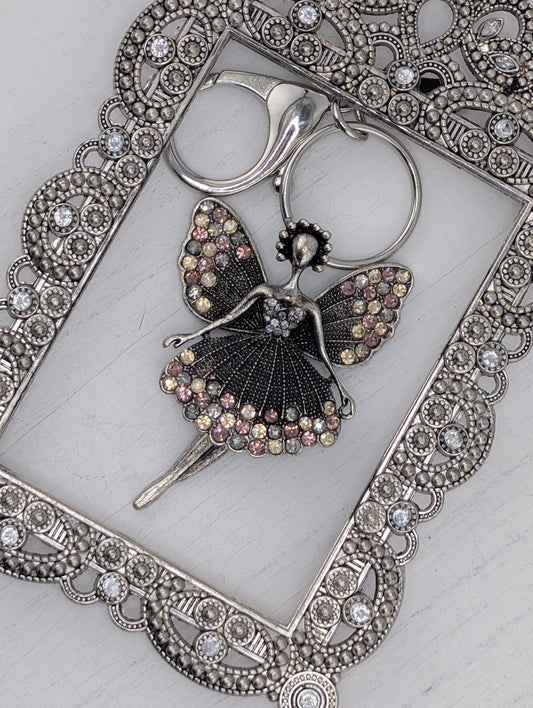 a silver-colored pendant with a butterfly design, adorned with sparkling rhinestones or crystals. The pendant is placed within an ornate, decorative metal frame, which adds an elegant touch to the overall presentation.