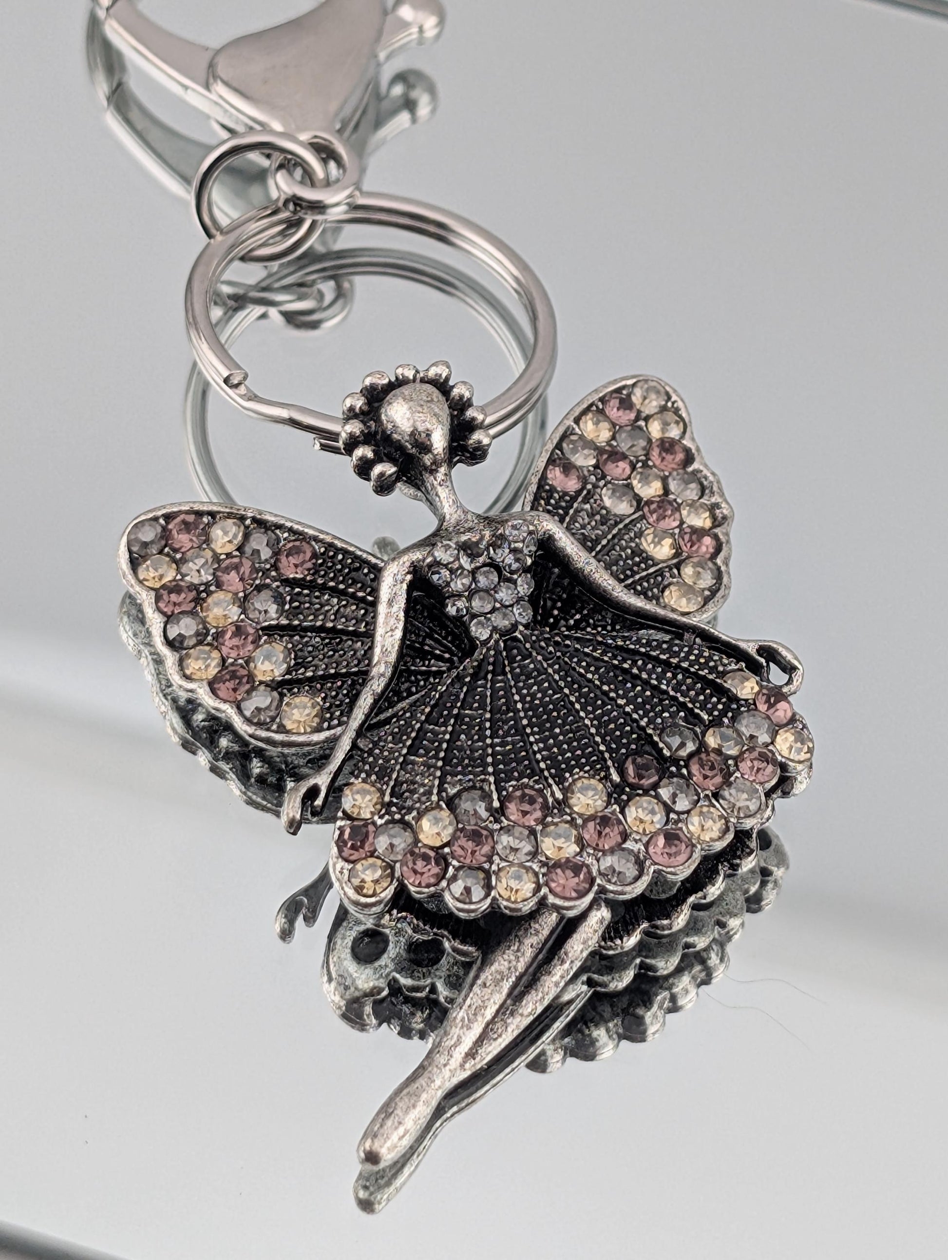 A silver-colored keychain with a decorative design featuring a butterfly-like figure with intricate details and sparkling gemstones.