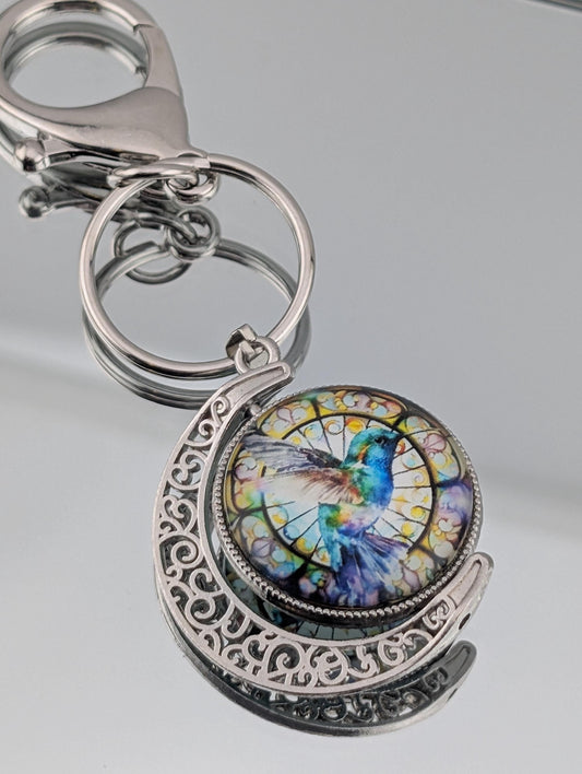 A keychain with a decorative metal frame and a circular pendant featuring a colorful hummingbird design.