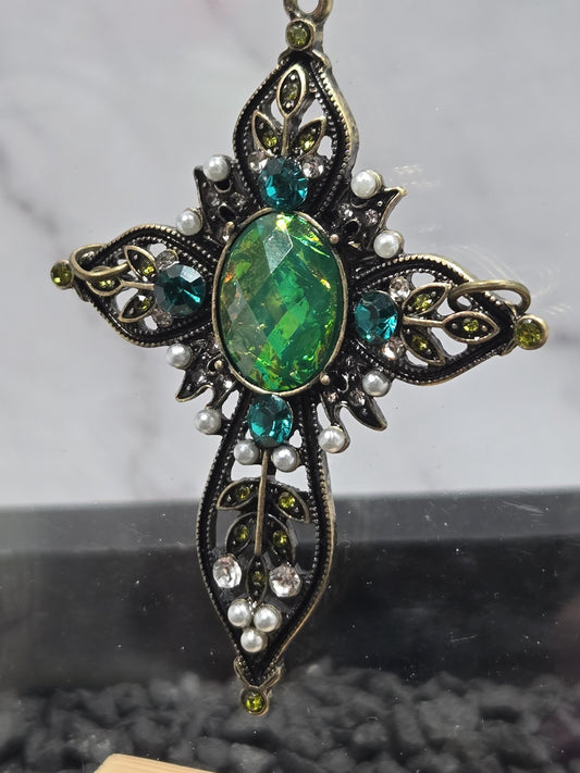 A decorative pendant with a large green gemstone surrounded by smaller gemstones, pearls, and leaves.