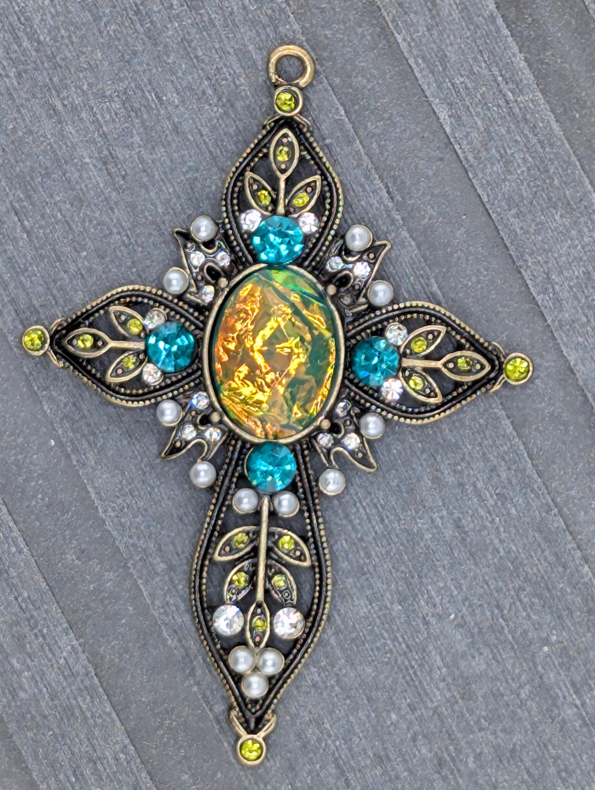 a decorative piece of jewelry with a large oval-shaped gemstone surrounded by smaller gemstones, pearls, and leaves.