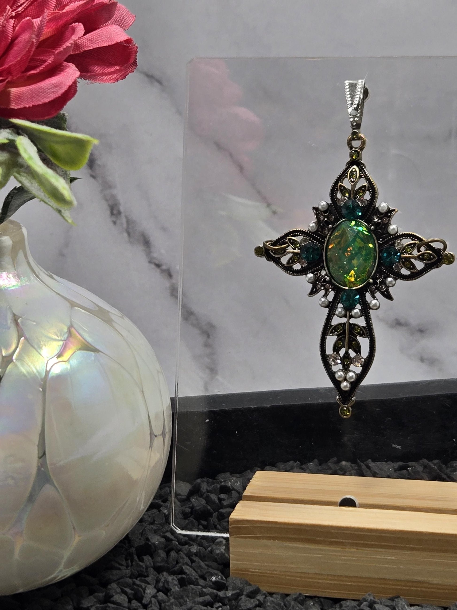 a decorative piece of jewelry with a green gemstone, displayed on a glass surface.