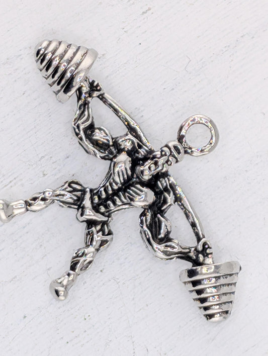 A silver-colored metal charm in the shape of a skeleton, holding two weights in its hands.