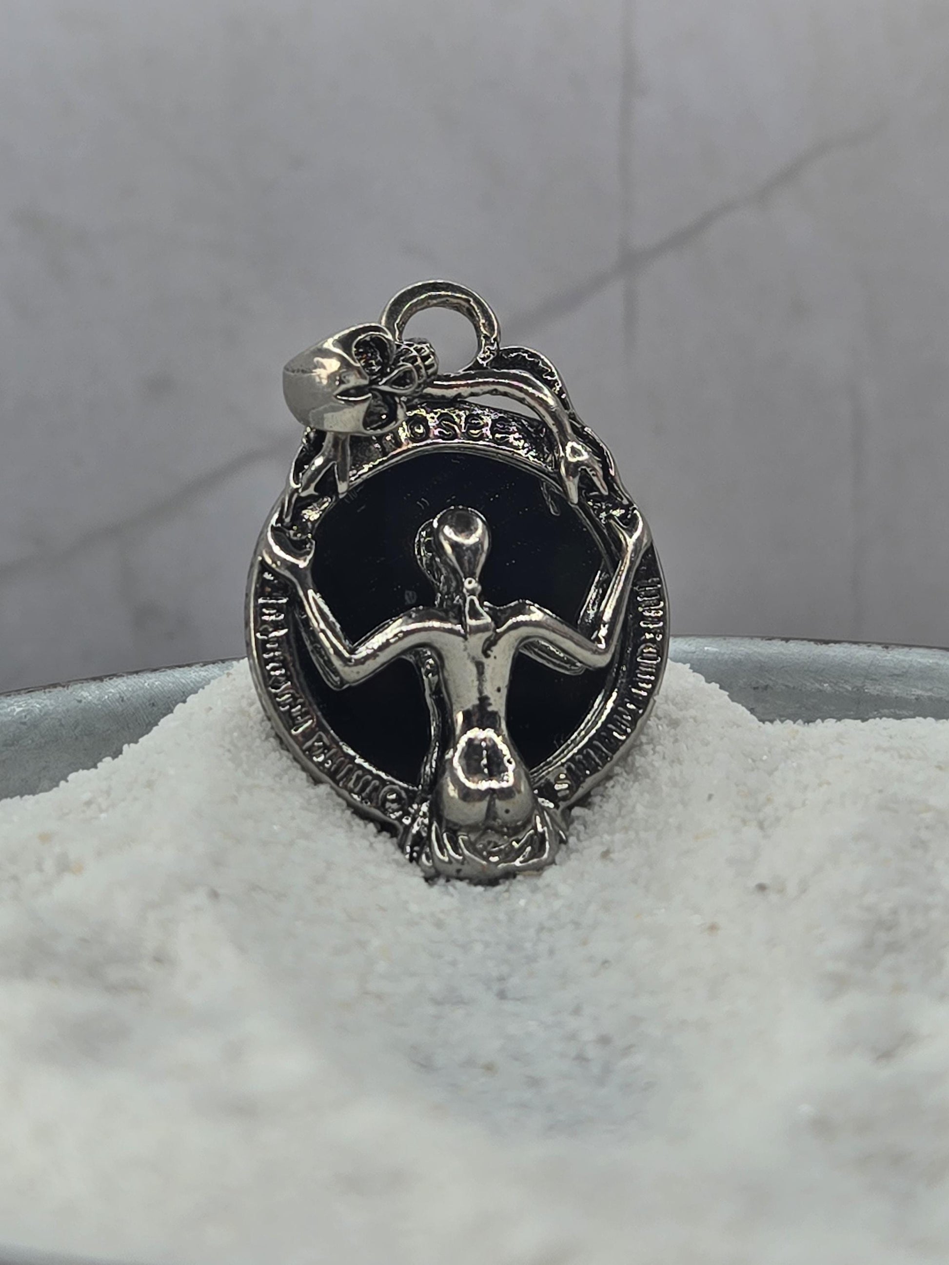 A silver-colored charm or pendant with an intricate design, resting on a white surface.