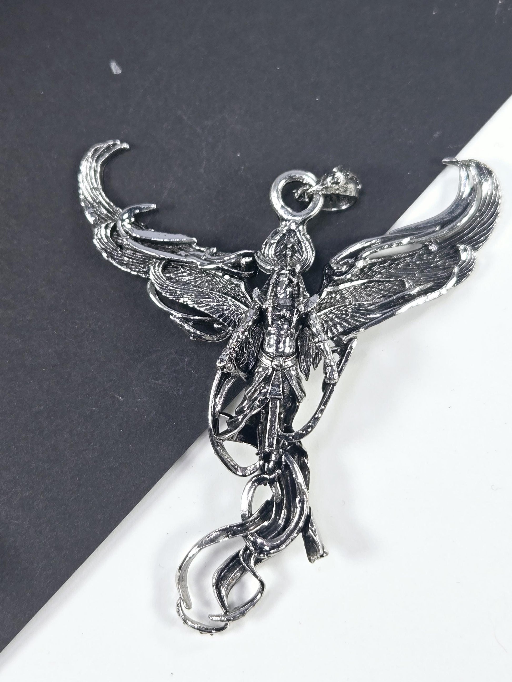 A silver-colored metal pendant in the shape of a bird, with intricate details and a decorative design.