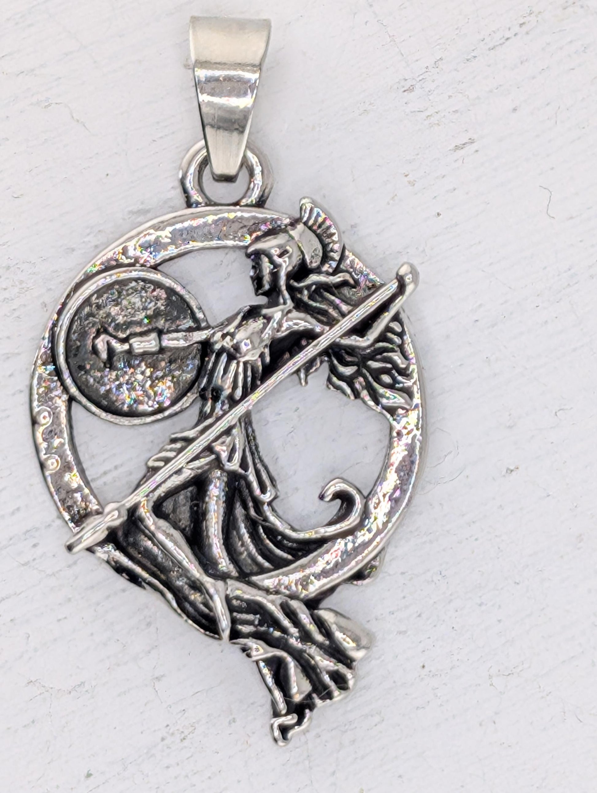 A silver-colored pendant featuring an intricate design of a woman holding a shield and a sword.