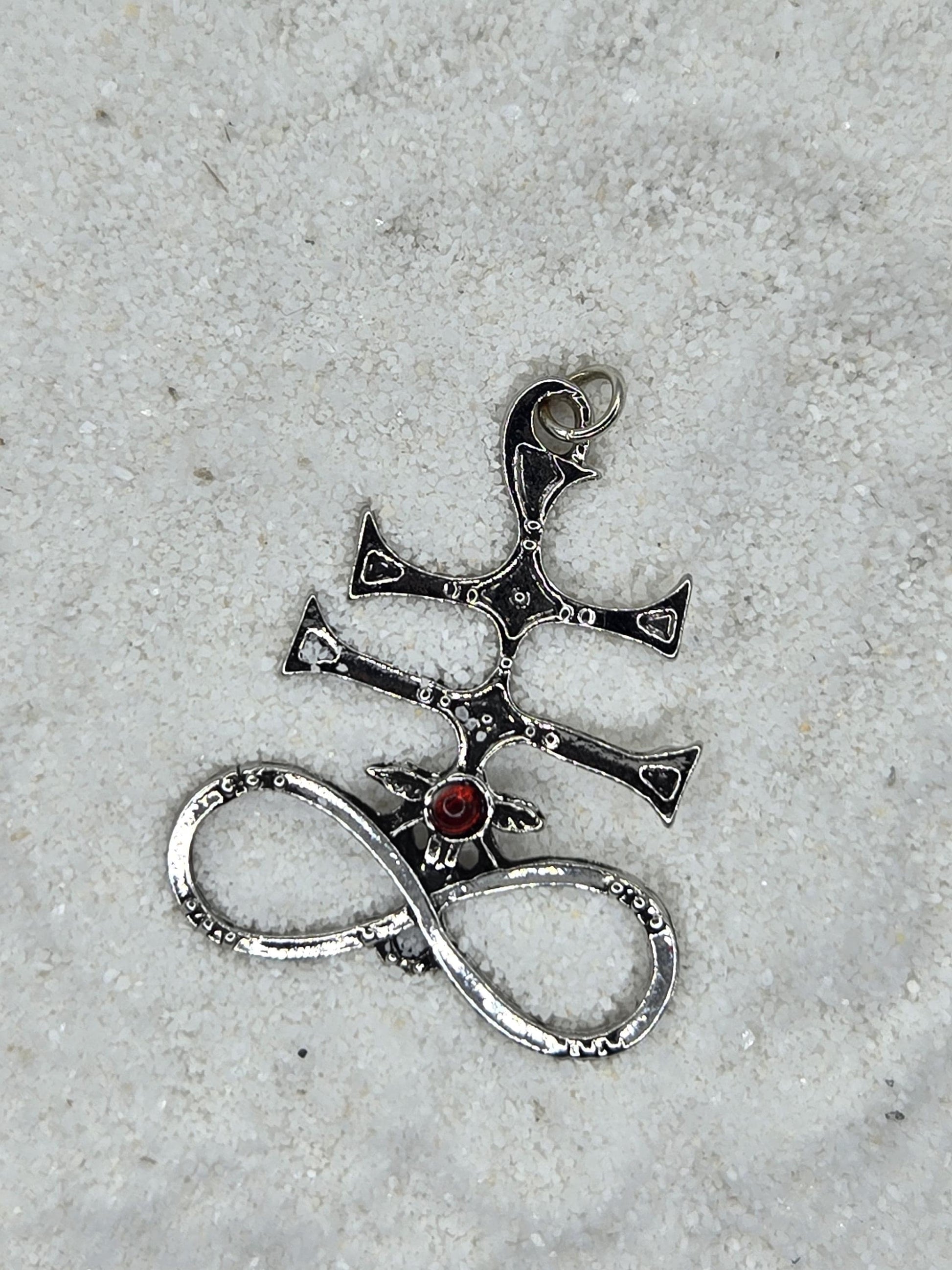A silver pendant with a red gemstone, lying on a white surface.