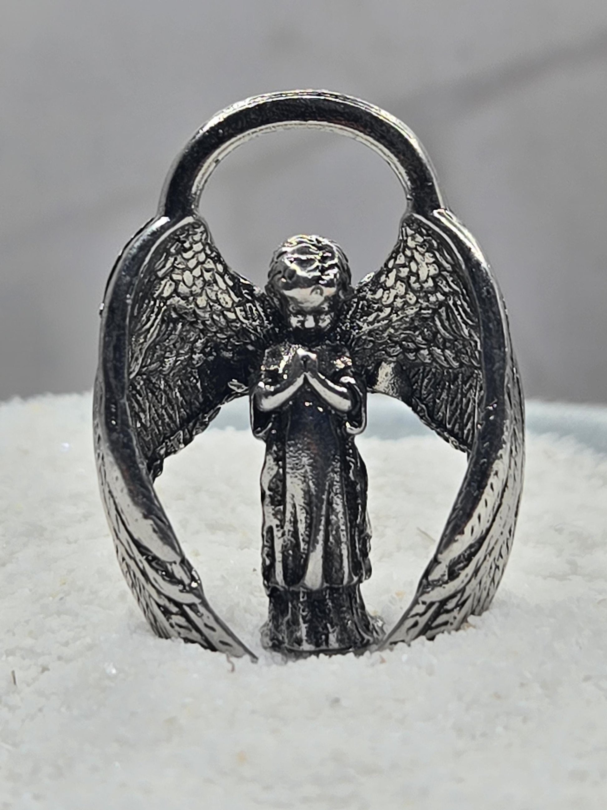 A silver-colored metal ring with an intricate design of wings and a central figure, possibly an angel or deity.