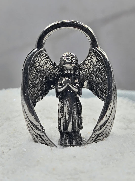 A silver-colored metal ring with an intricate design of wings and a central figure, possibly an angel or deity.