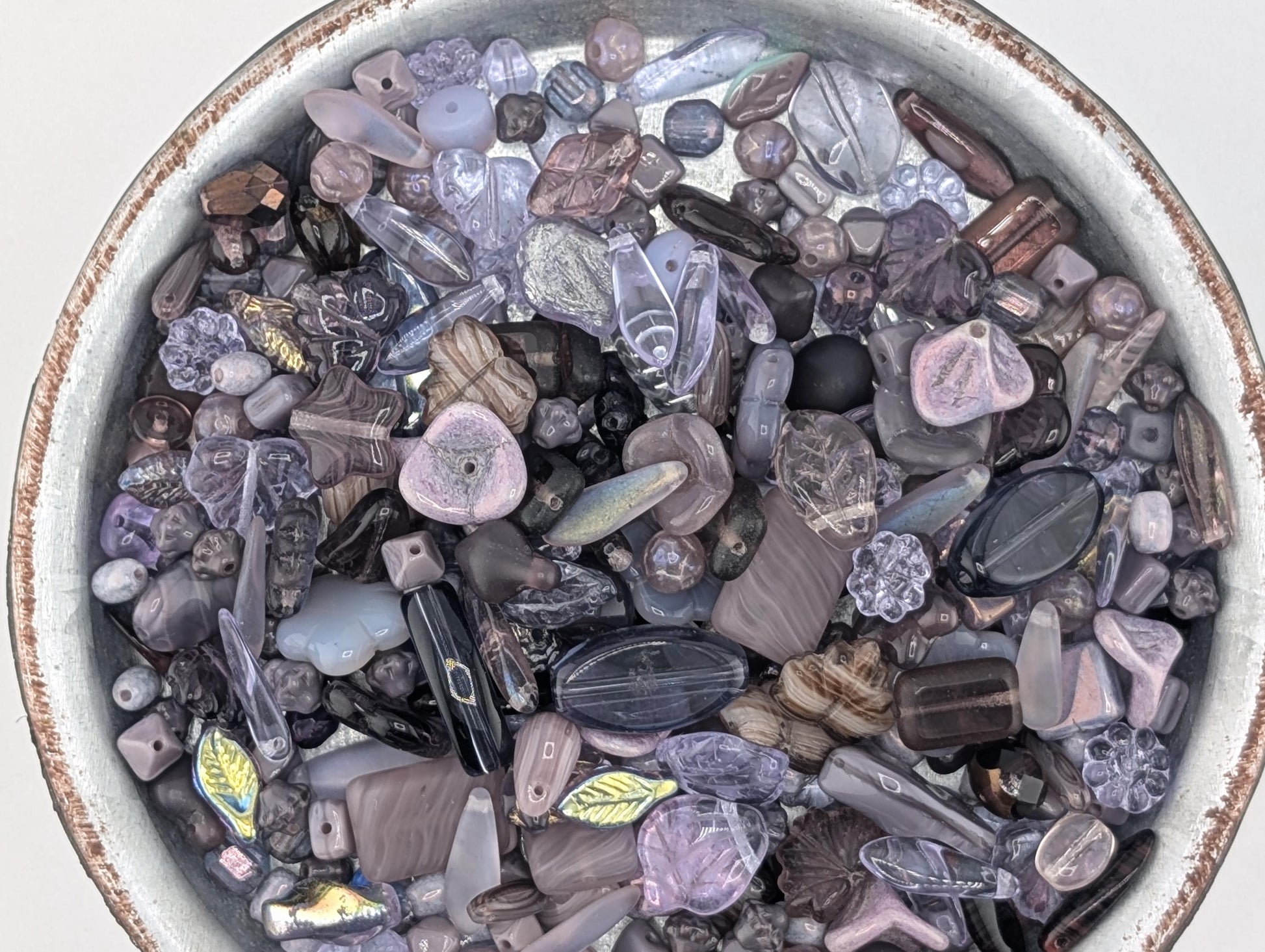a bowl filled with various colorful beads, including clear, purple, and black beads, as well as some larger beads with unique shapes and designs.