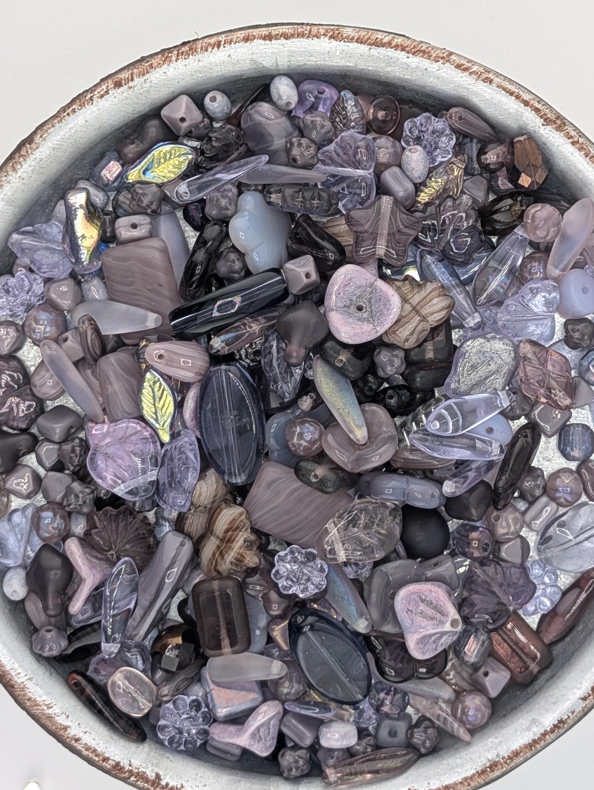 a bowl filled with various colored glass beads, including shades of purple, blue, and gray.