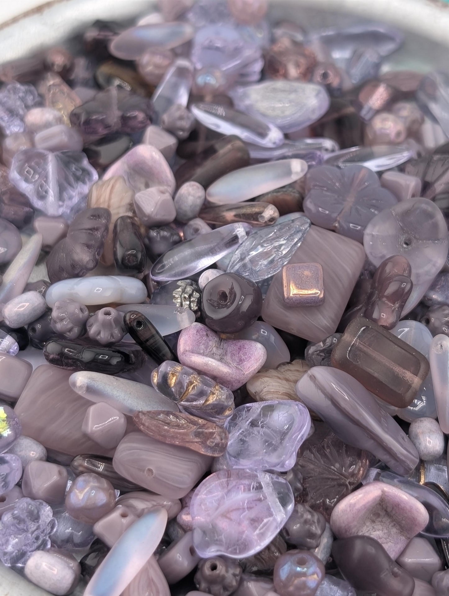The image is a close-up of a collection of various glass beads and stones in shades of purple and pink.