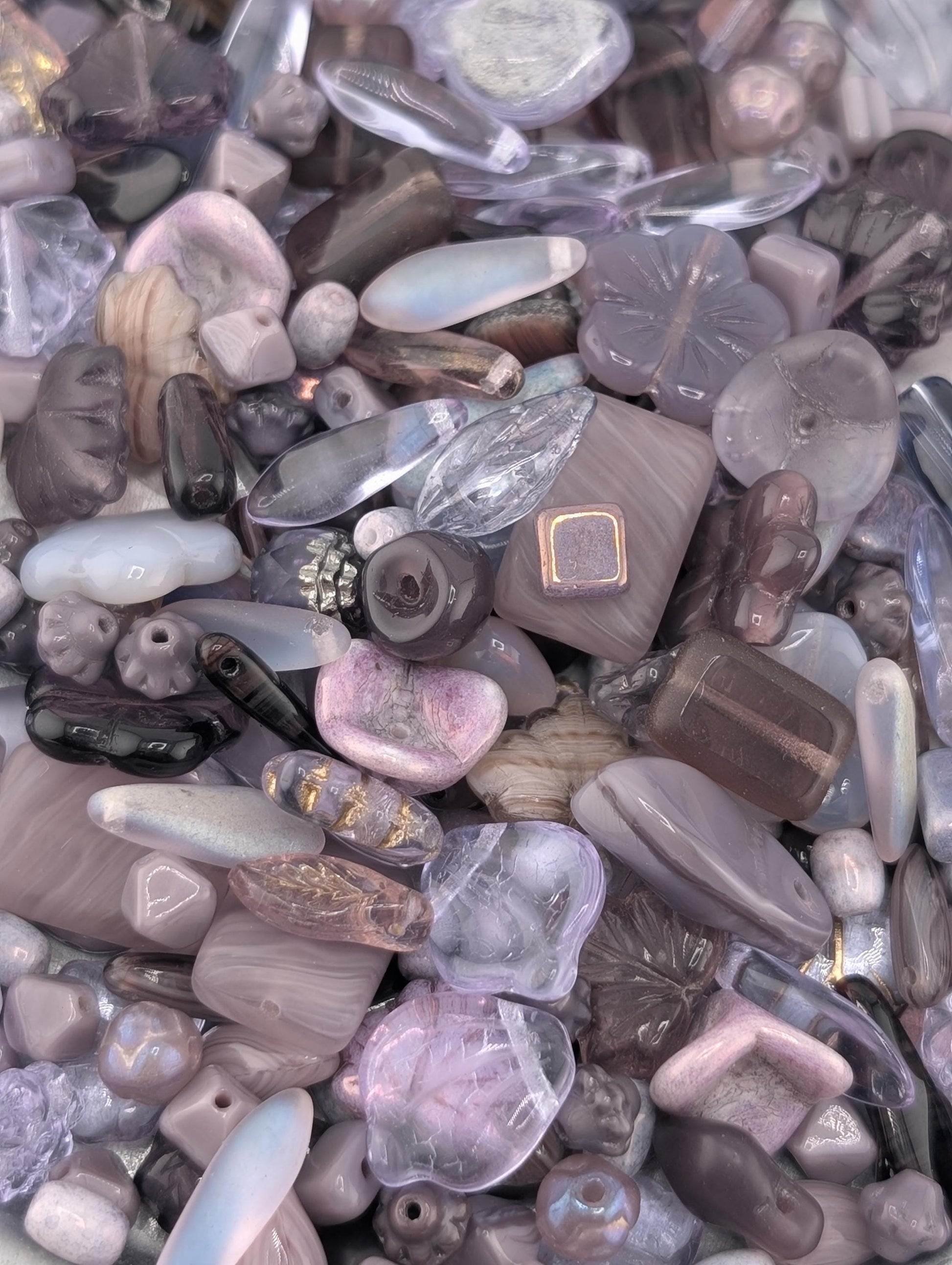 The image is a close-up of various glass beads and gemstones, including clear, purple, and brown hues, scattered together.