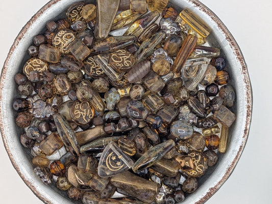 A bowl filled with various colored glass beads, including clear, brown, and multicolored pieces.