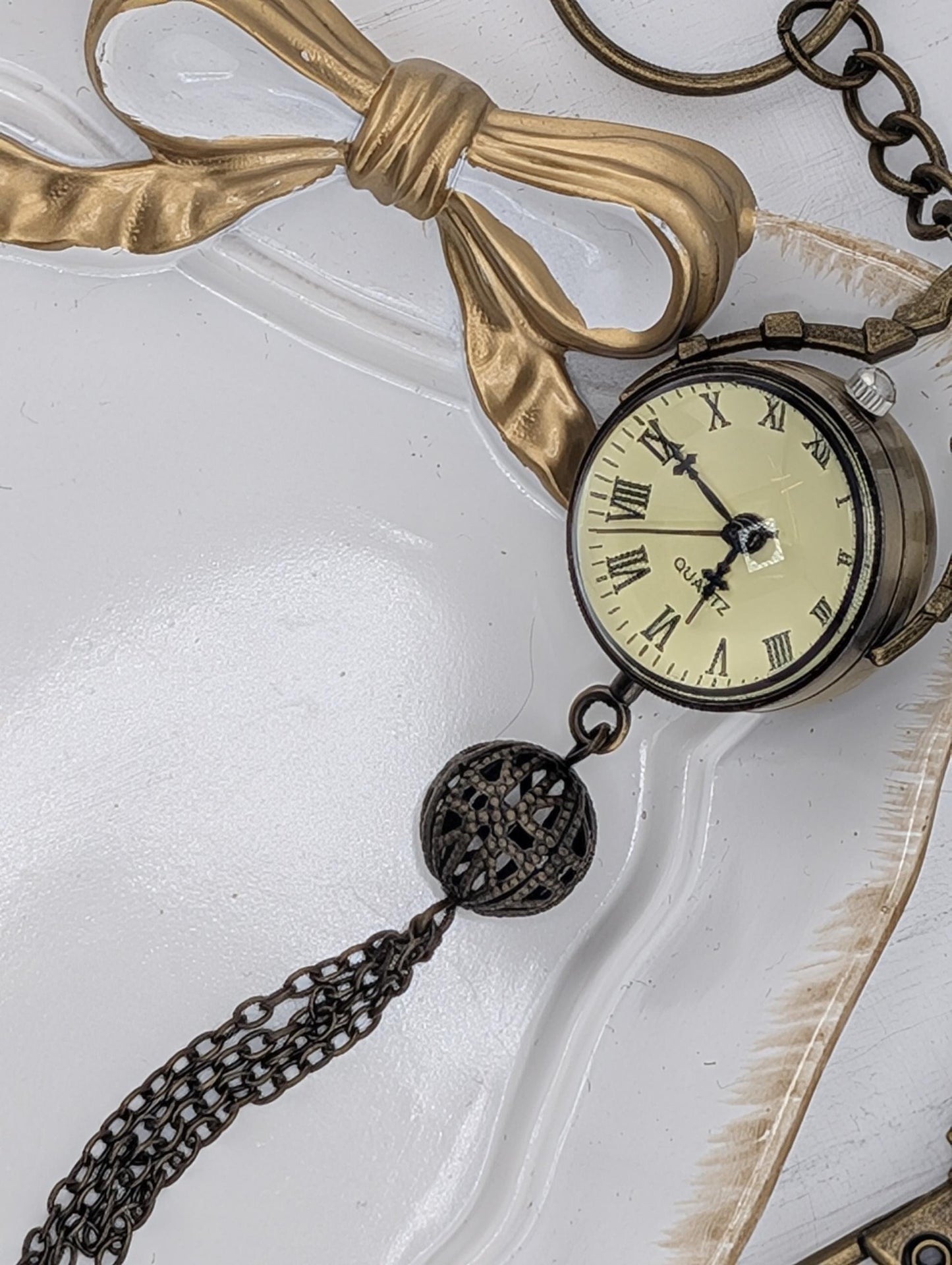 An antique pocket watch with a gold-colored ribbon and chain is displayed on a white surface.