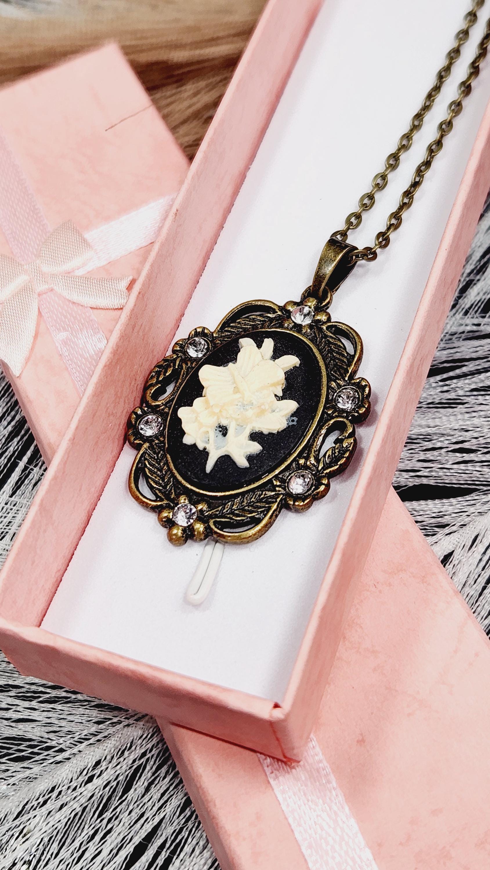 A decorative necklace with a pendant featuring a floral design is displayed in a pink jewelry box.