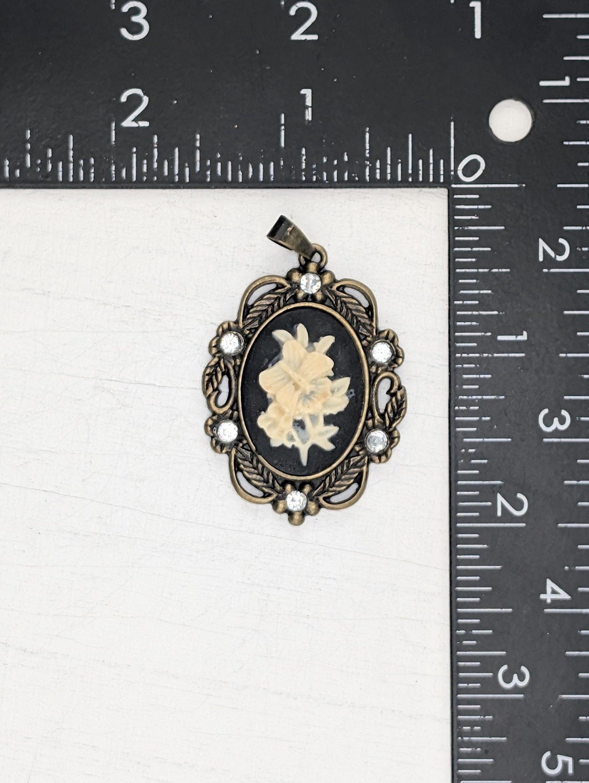 A pendant with a floral design and a small flower inside, placed next to a ruler for size comparison.