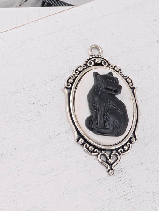 A silver-toned pendant featuring a black cat sitting inside an oval frame with an ornate border.