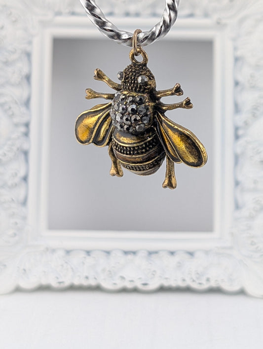 A decorative pendant in the shape of a bee, with intricate details and sparkling gemstones, is hanging from a chain.