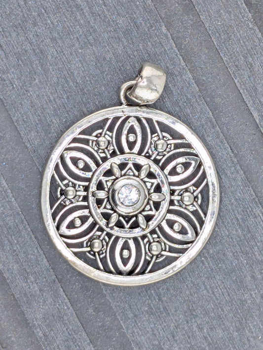 A silver pendant with an intricate design, featuring a central motif surrounded by smaller, symmetrical patterns.