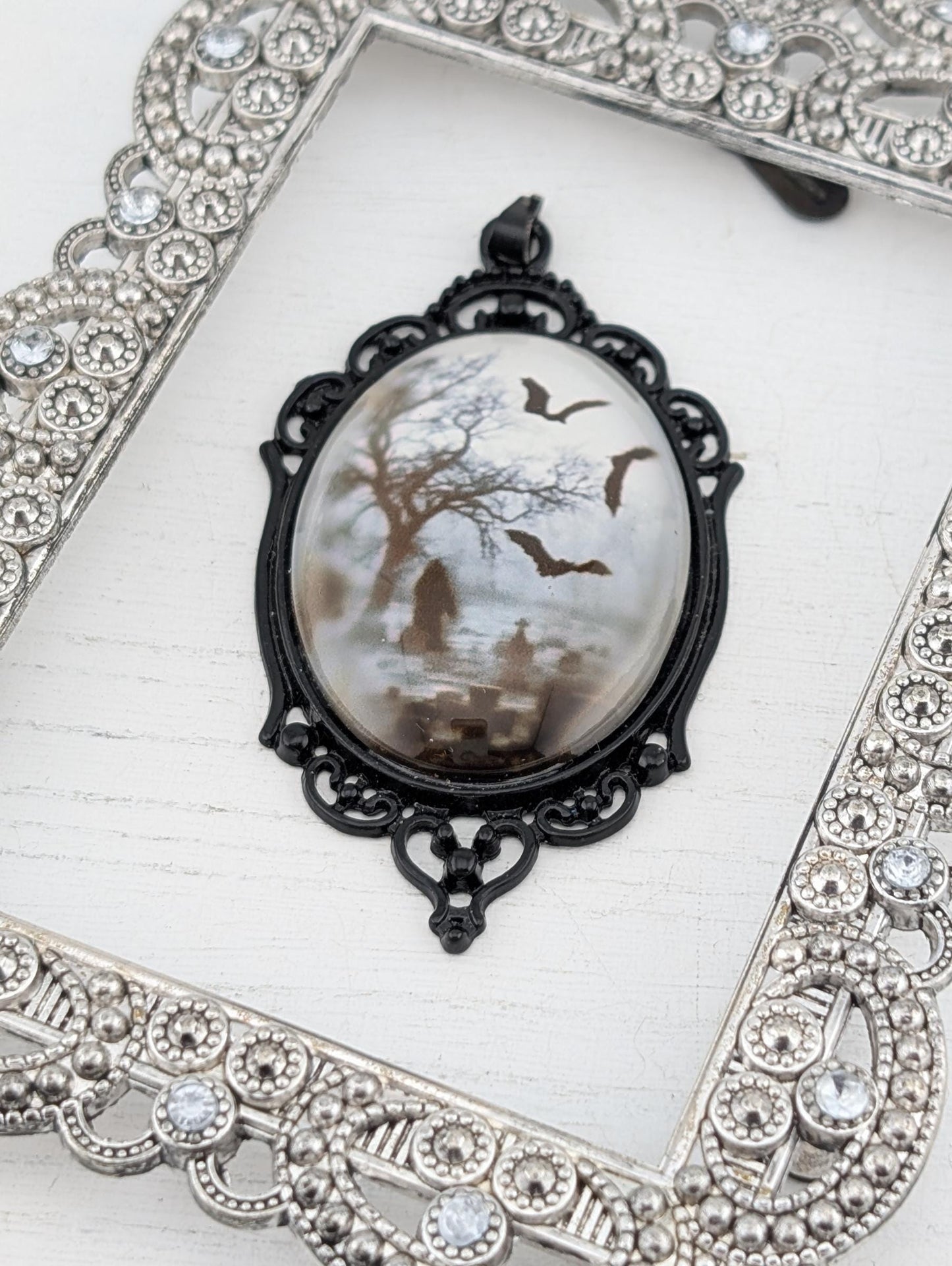 A pendant with a design featuring bats and a tree, displayed in an ornate silver frame.
