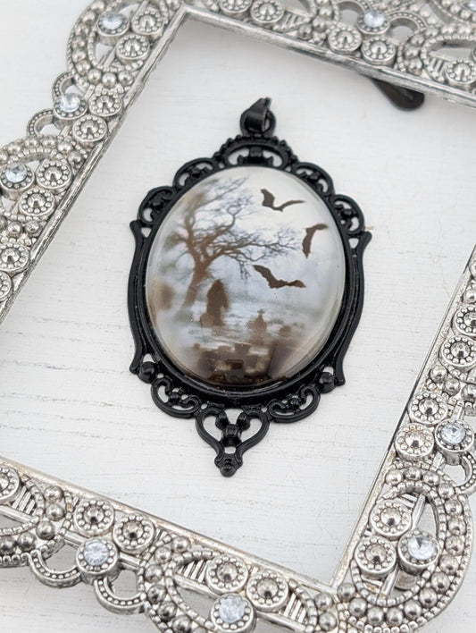 A pendant with a design featuring bats and a tree, displayed in an ornate silver frame.