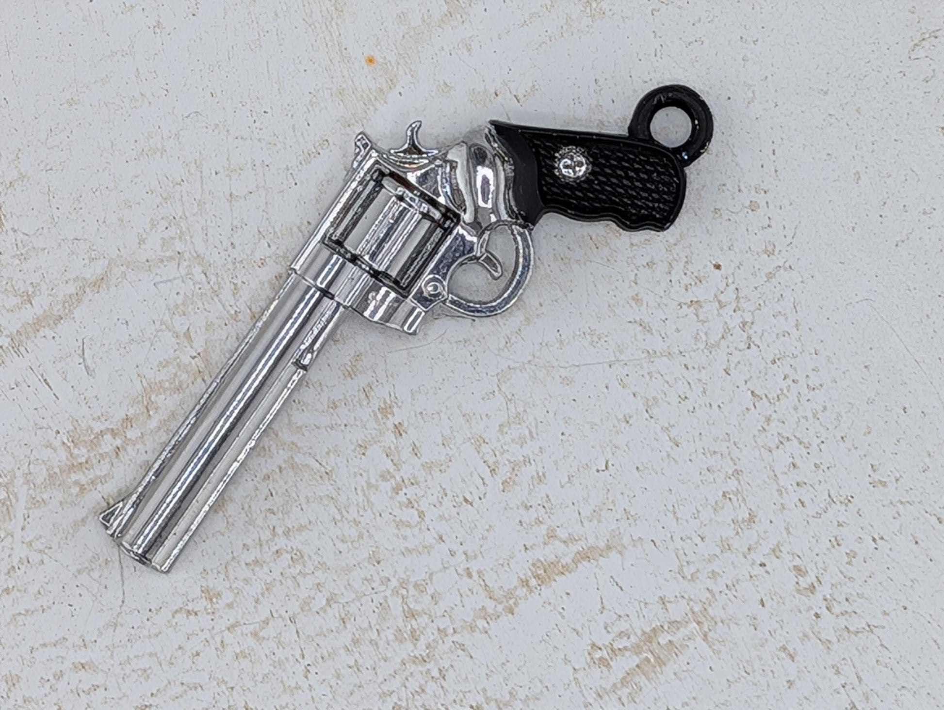A silver toy gun with a black grip is lying on a white surface.