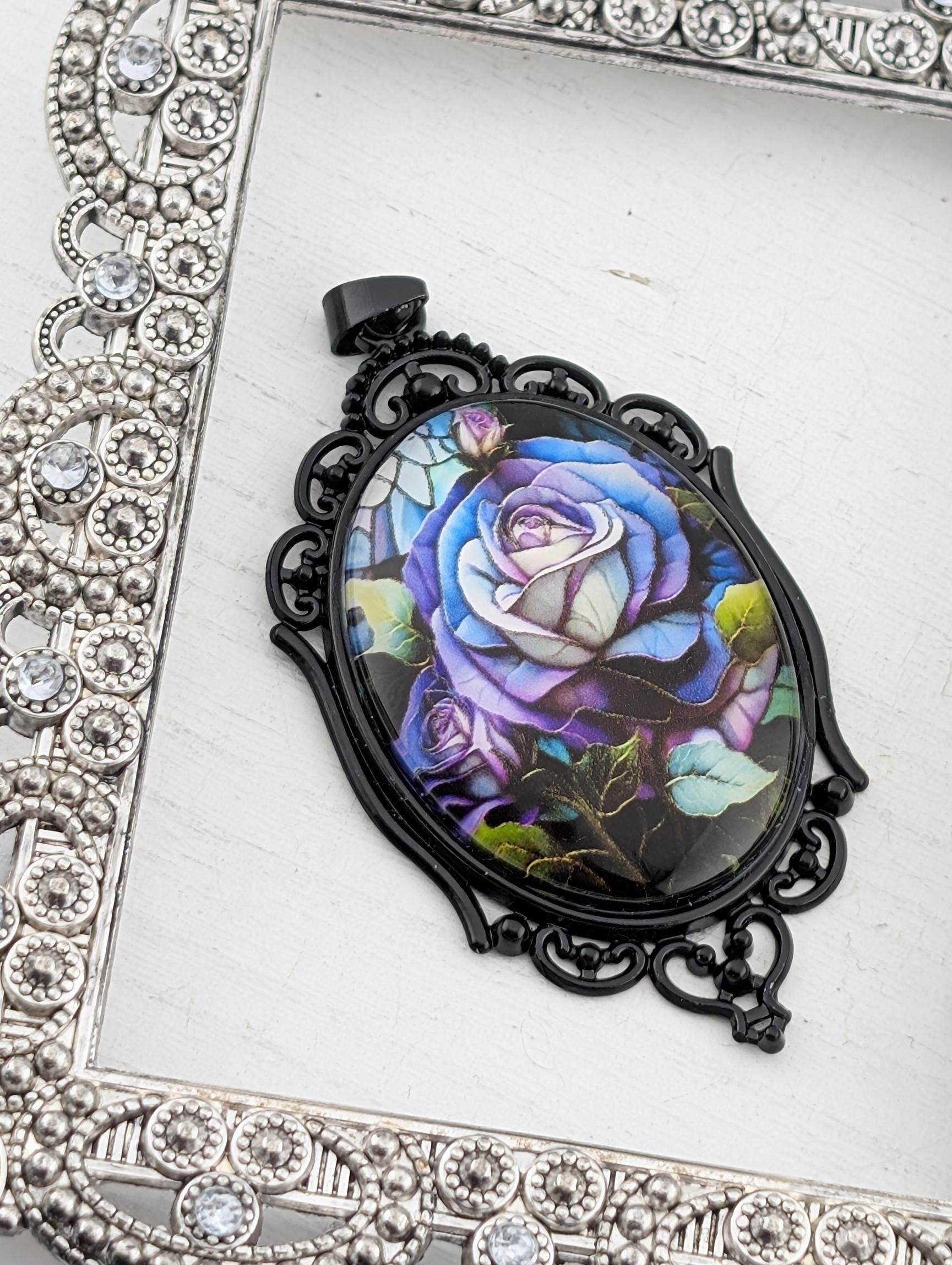 A decorative pendant featuring a vibrant, colorful rose design is displayed against a white background, framed by an ornate, silver-toned metal frame.