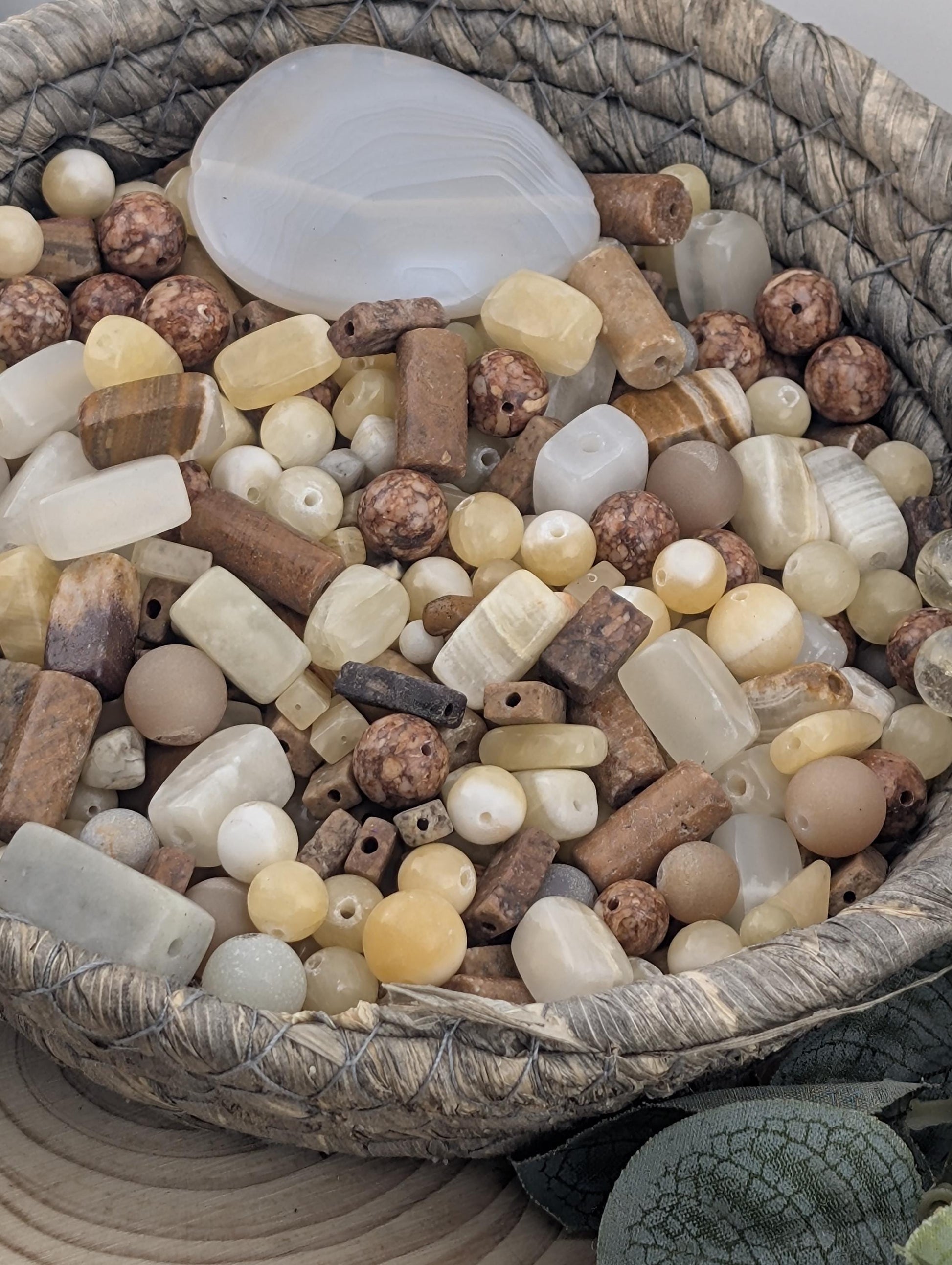 A woven basket filled with various beads and stones, including white, brown, and beige colors.
