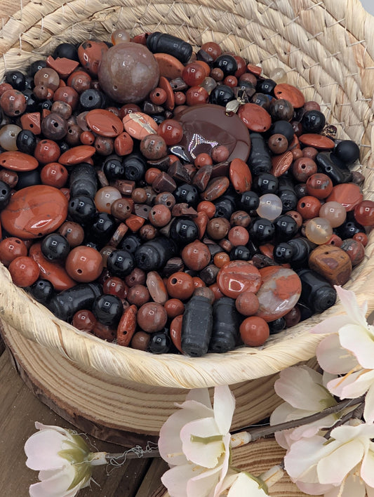 A woven basket filled with a variety of colorful beads, including red, black, and white beads, along with some flowers.