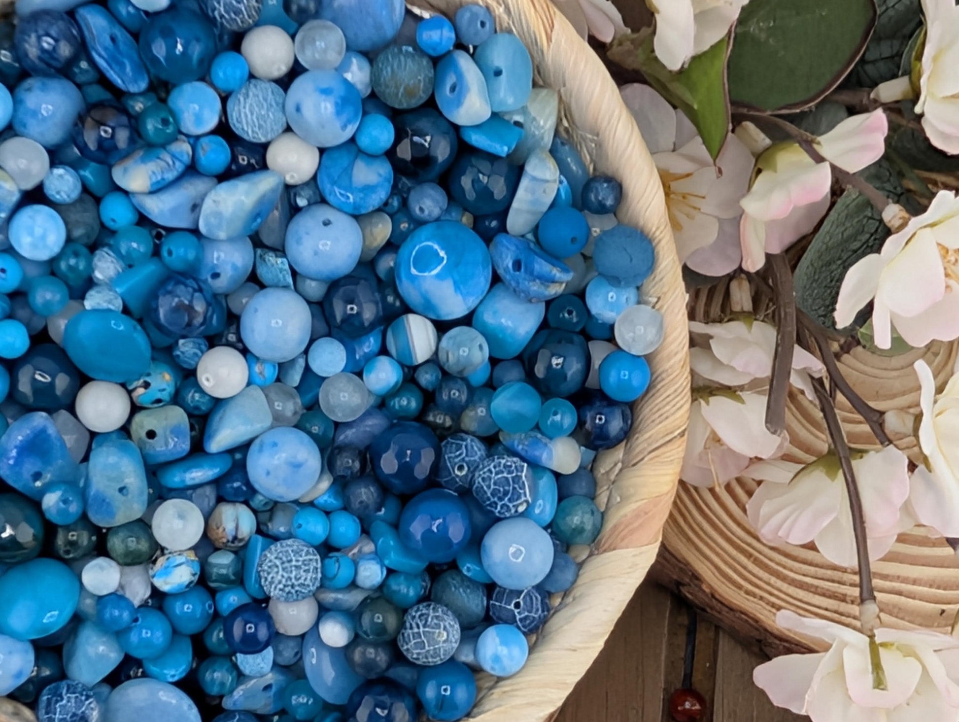 A bowl filled with various blue and white beads, with some flowers visible in the background.
