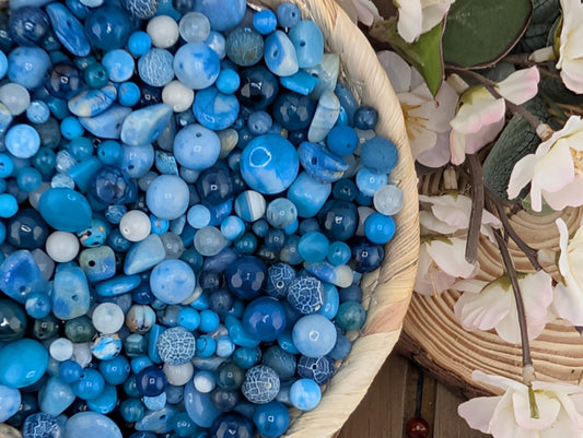 A bowl filled with various blue and white beads, with some flowers visible in the background.
