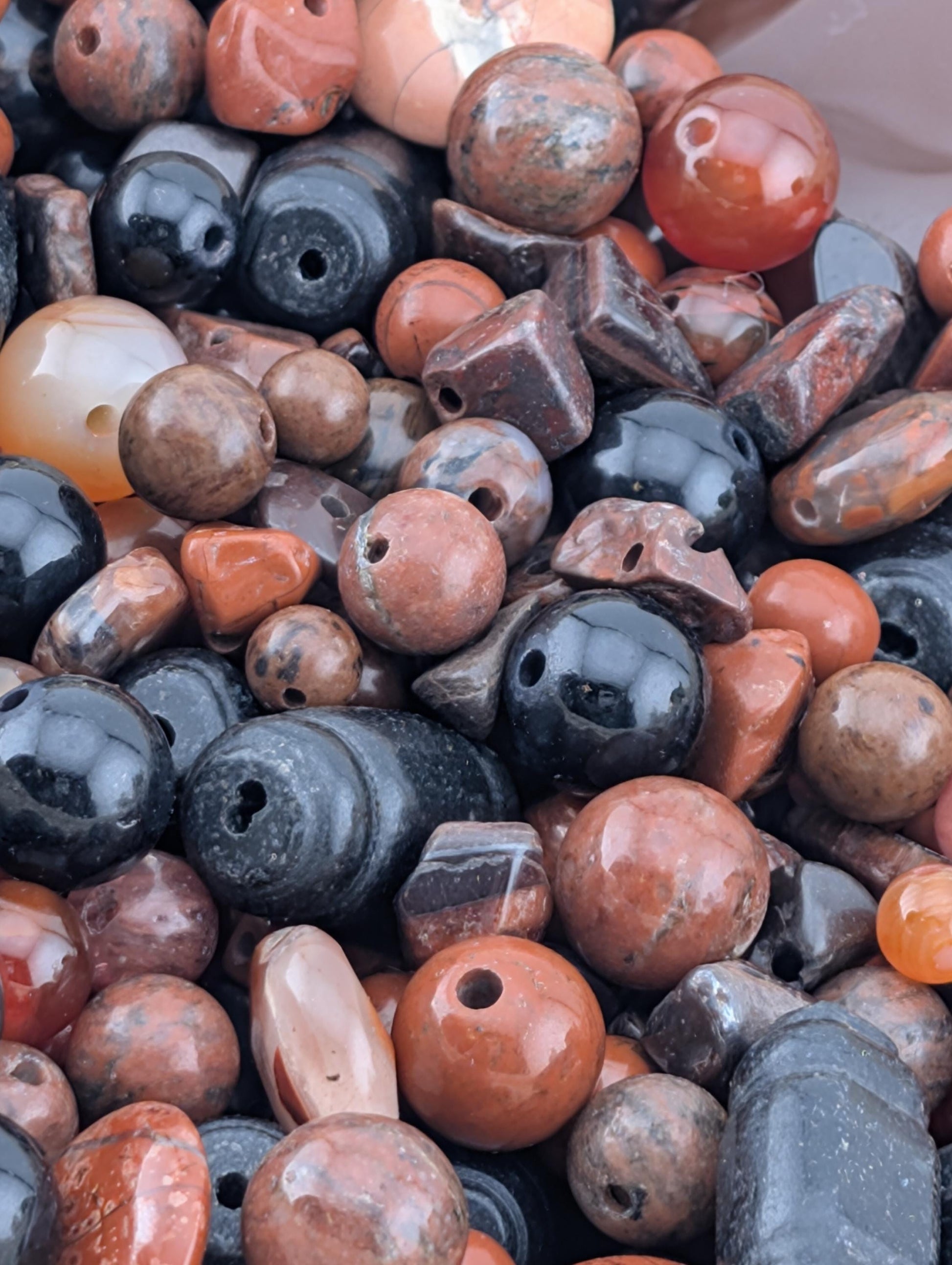 The image is a close-up of various colored beads and stones, including black, orange, and brown, scattered together.