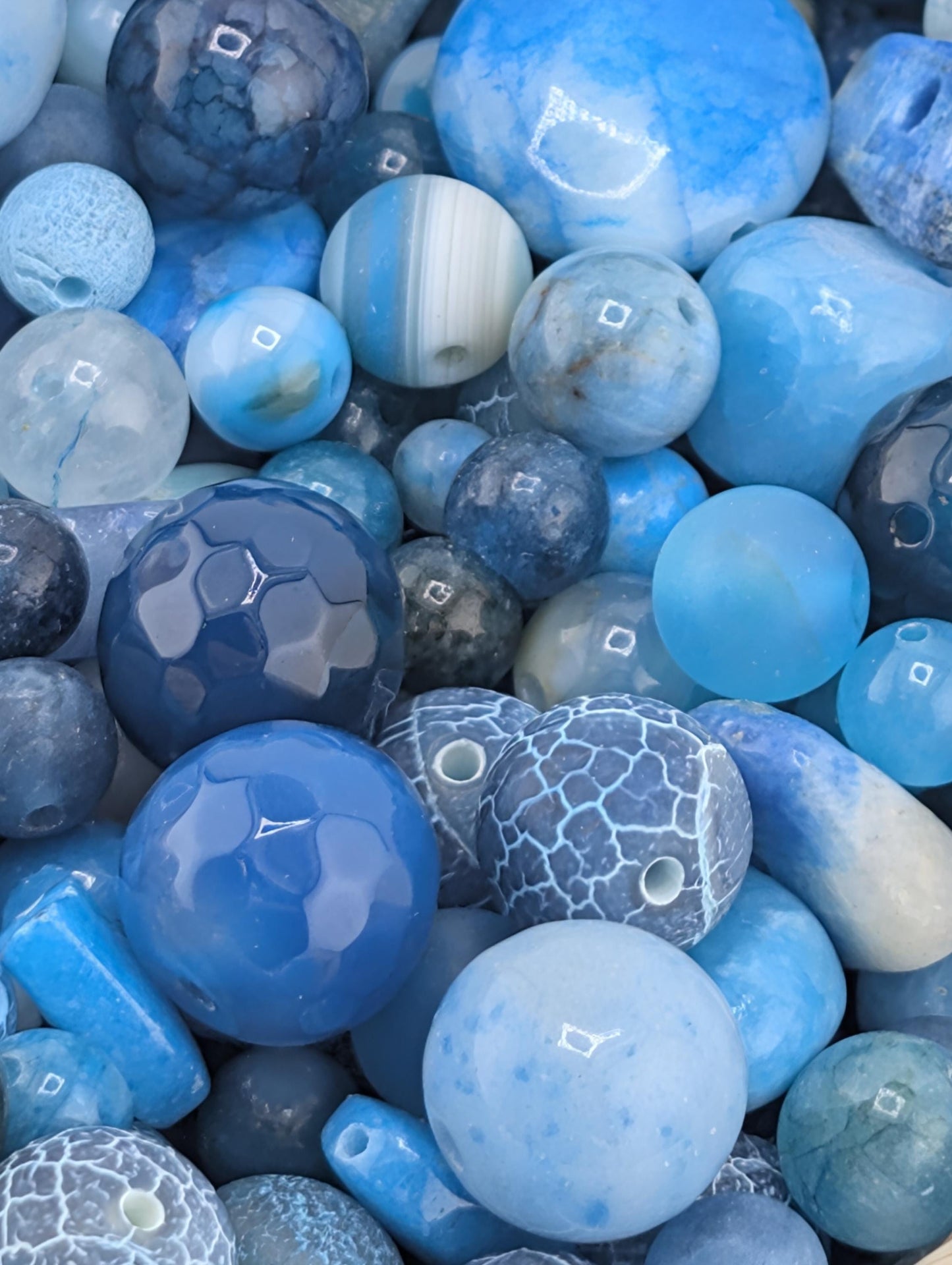a variety of blue and white beads, including round, hexagonal, and irregularly shaped pieces, arranged in a visually appealing manner.