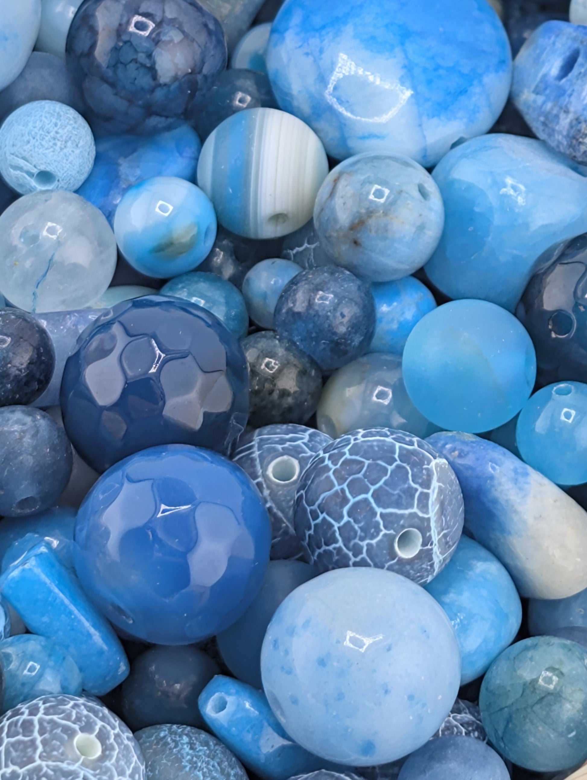 a variety of blue and white beads, including round, hexagonal, and irregularly shaped pieces, arranged in a visually appealing manner.