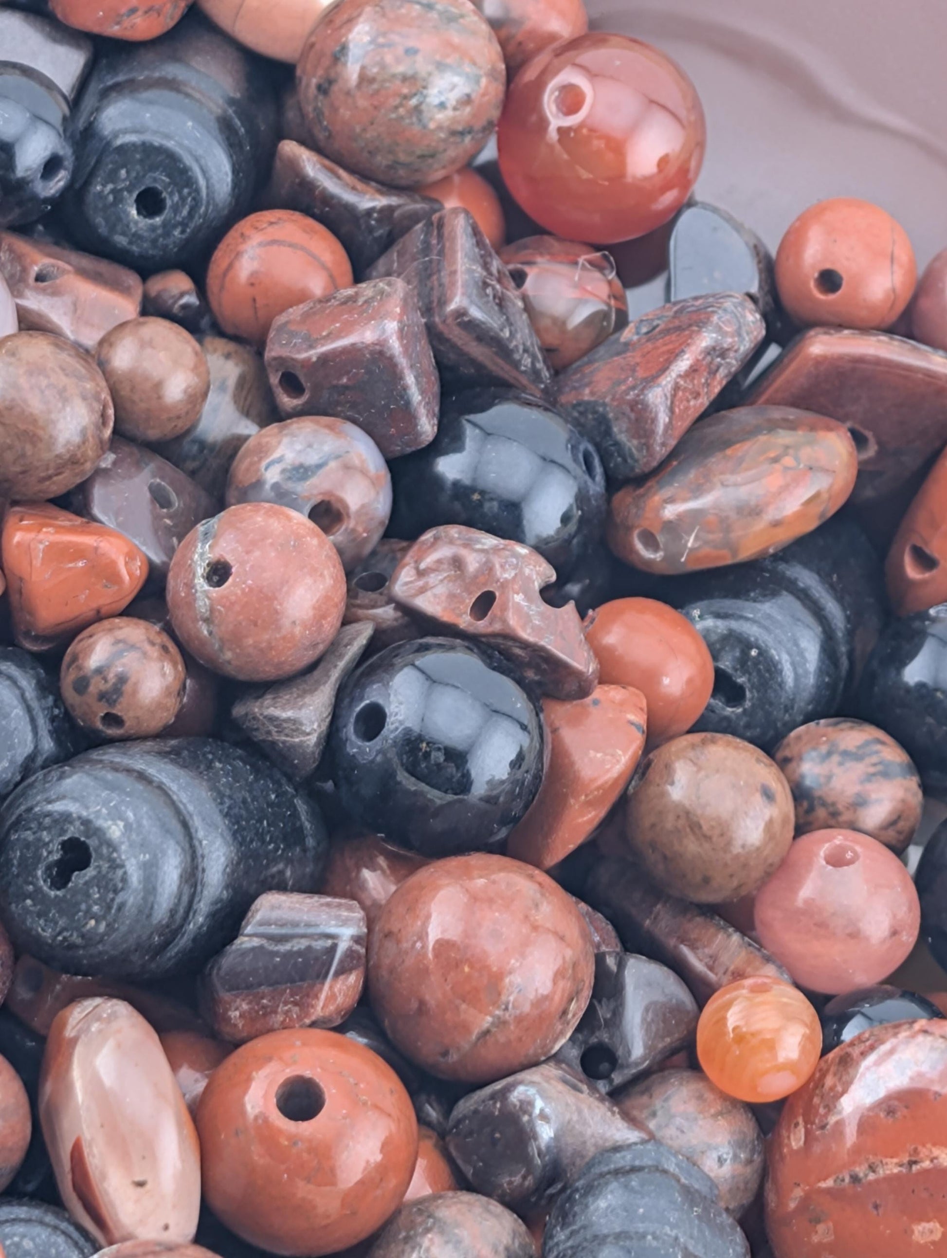 The image is a close-up of various colorful beads and stones, including shades of orange, black, and brown.