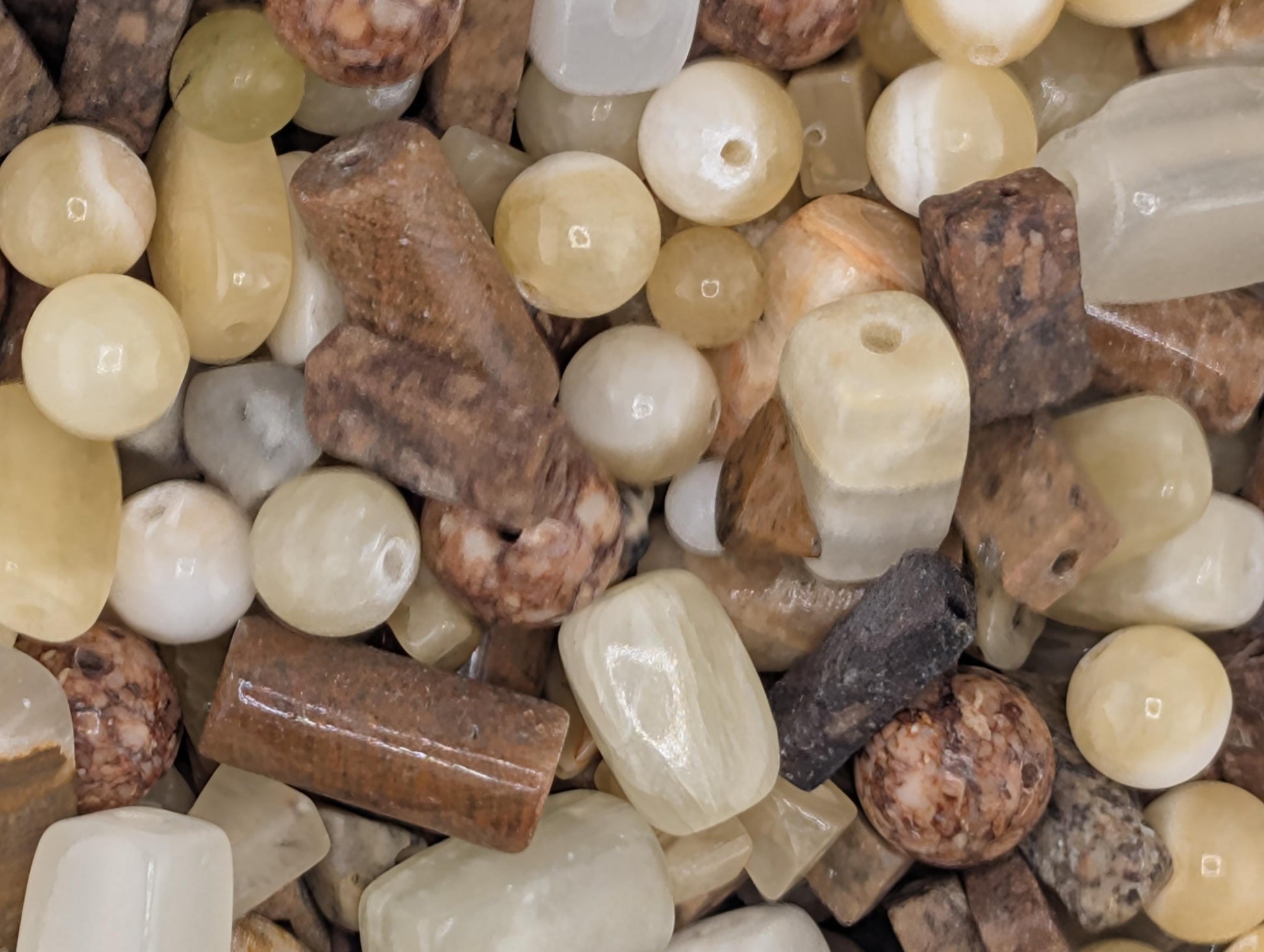 The image is a close-up of various natural stones and minerals, including beads, crystals, and other small, irregularly shaped objects.