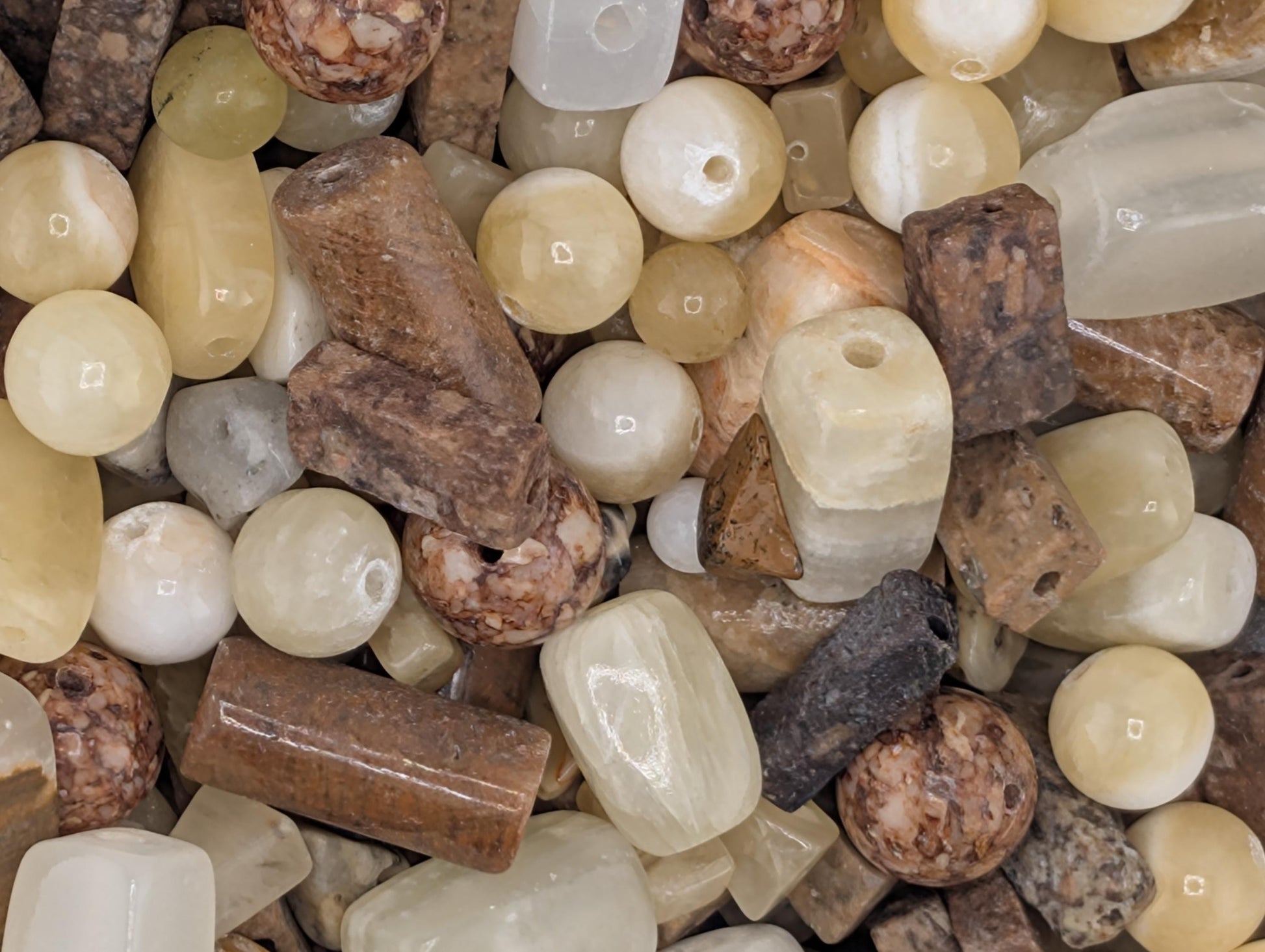 The image is a close-up of various natural stones and minerals, including crystals, beads, and other geological elements, arranged in a visually appealing manner.