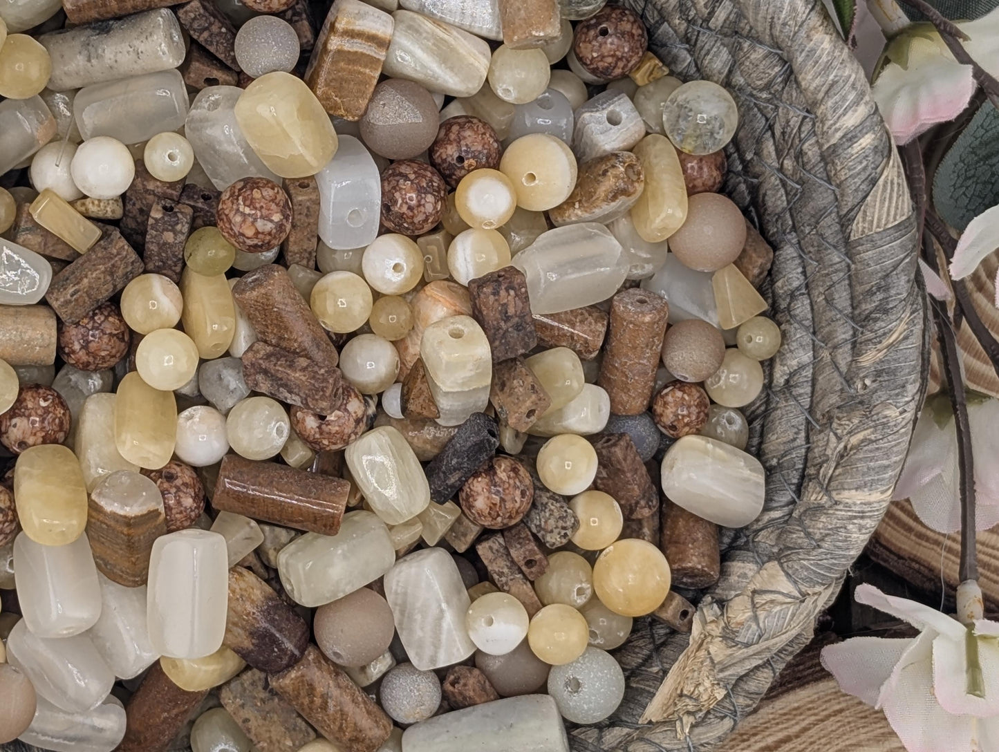 A close-up image of a variety of colorful beads and stones, including white, brown, and beige, arranged in a basket or container.