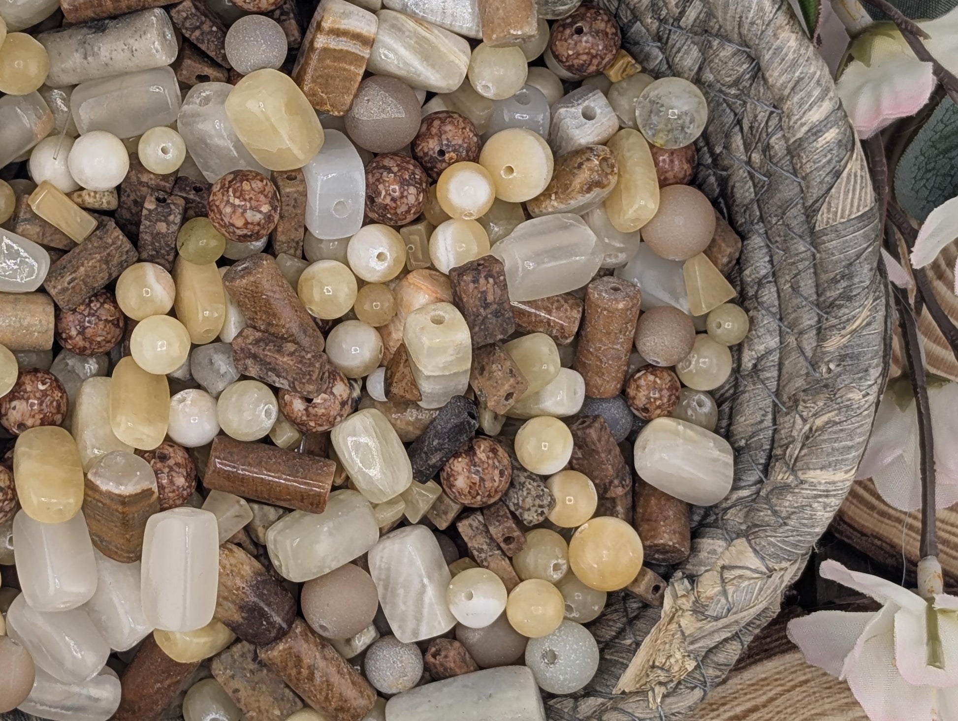 A close-up image of a variety of colorful beads and stones, including white, brown, and beige, arranged in a basket or container.