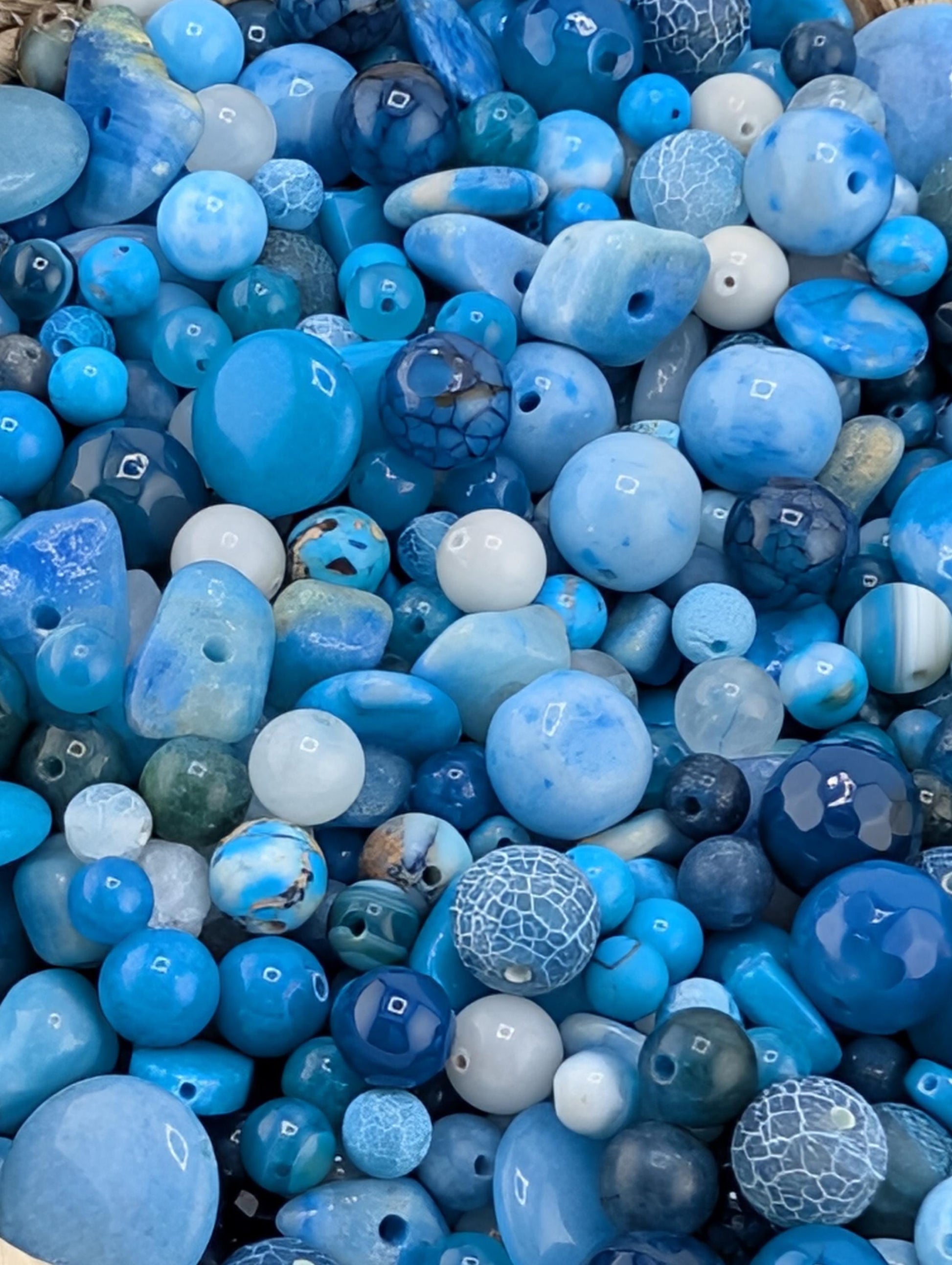 The image is a close-up of various blue and white beads, including glass beads and stone beads, arranged in a visually appealing manner.