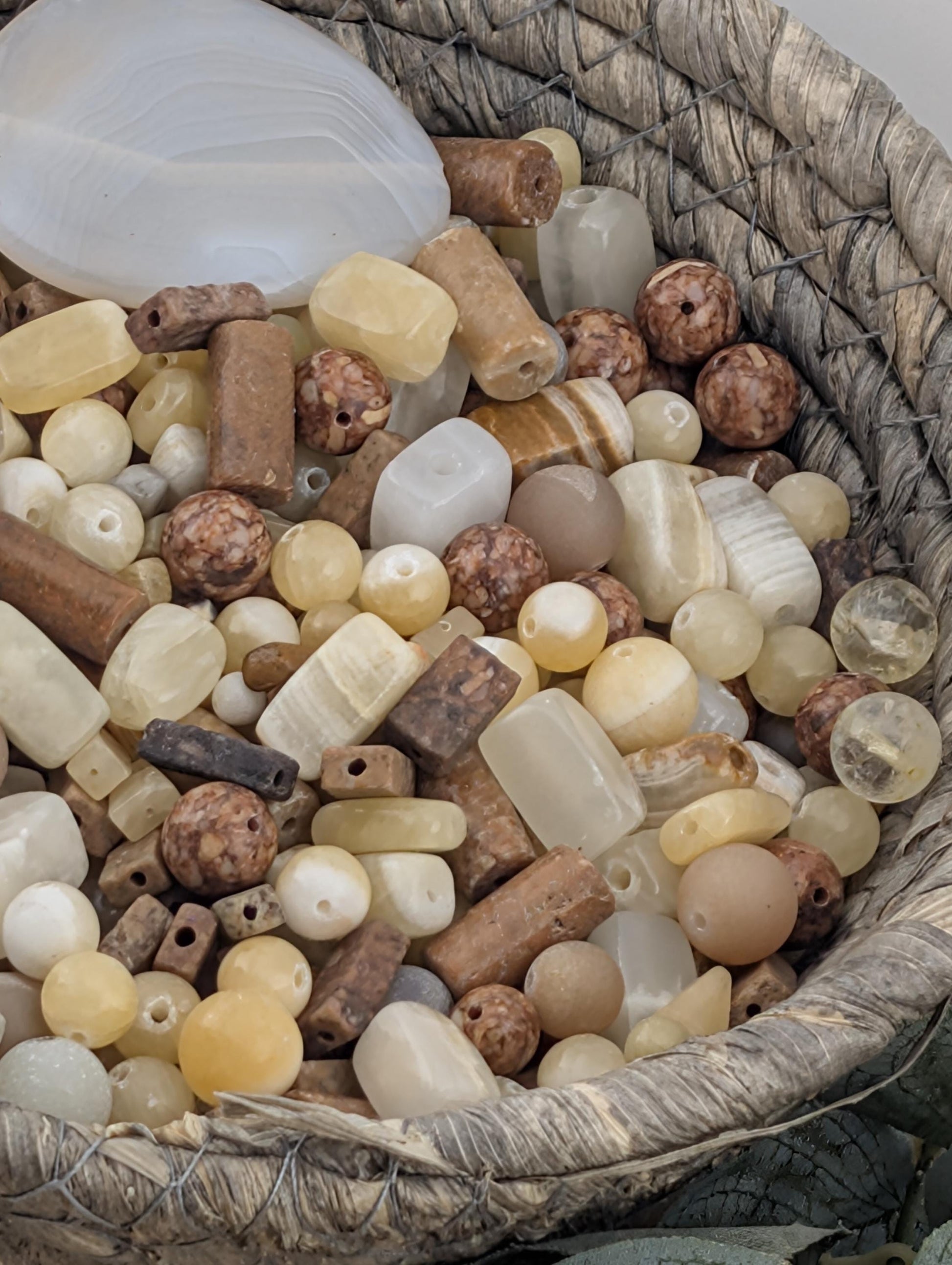 A woven basket filled with various beads and stones, including white, brown, and beige colors.