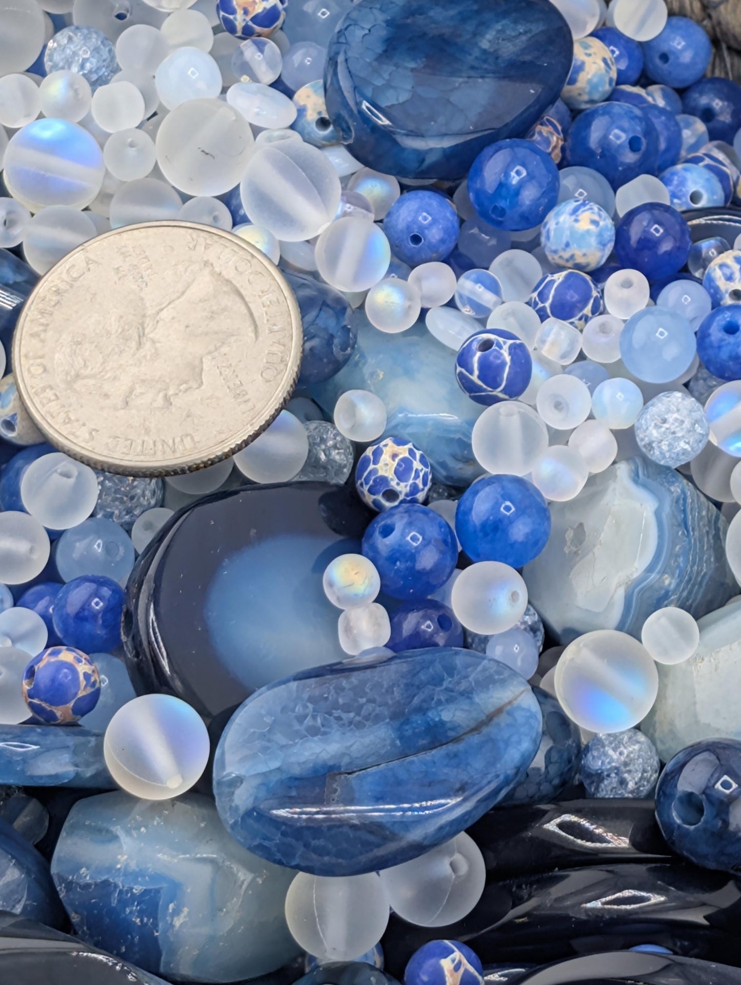 The image is a close-up of various blue and white beads, stones, and coins, creating a visually appealing and colorful composition.
