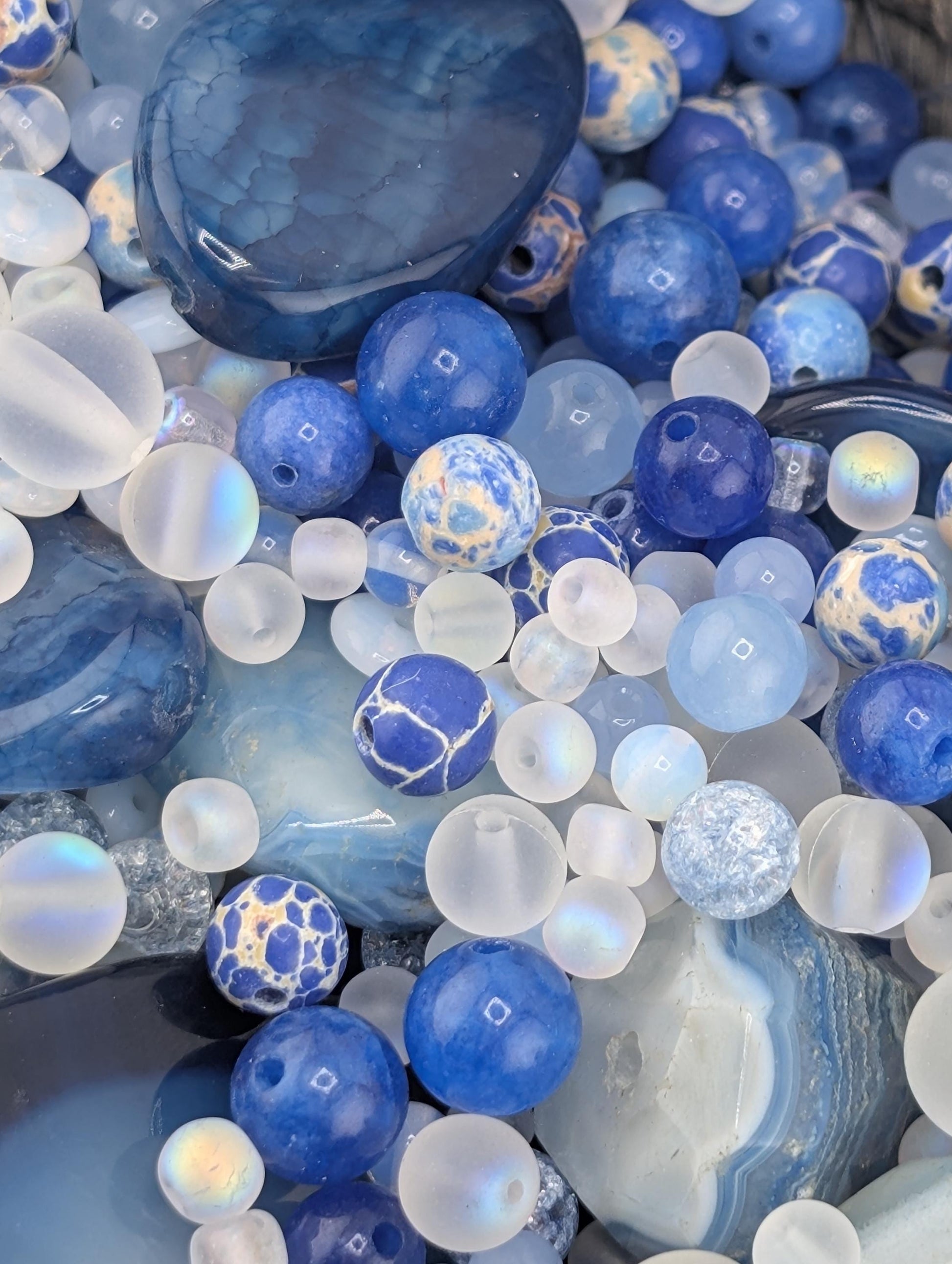 The image is a close-up of various blue and white beads, stones, and crystals, creating a visually appealing and colorful composition.