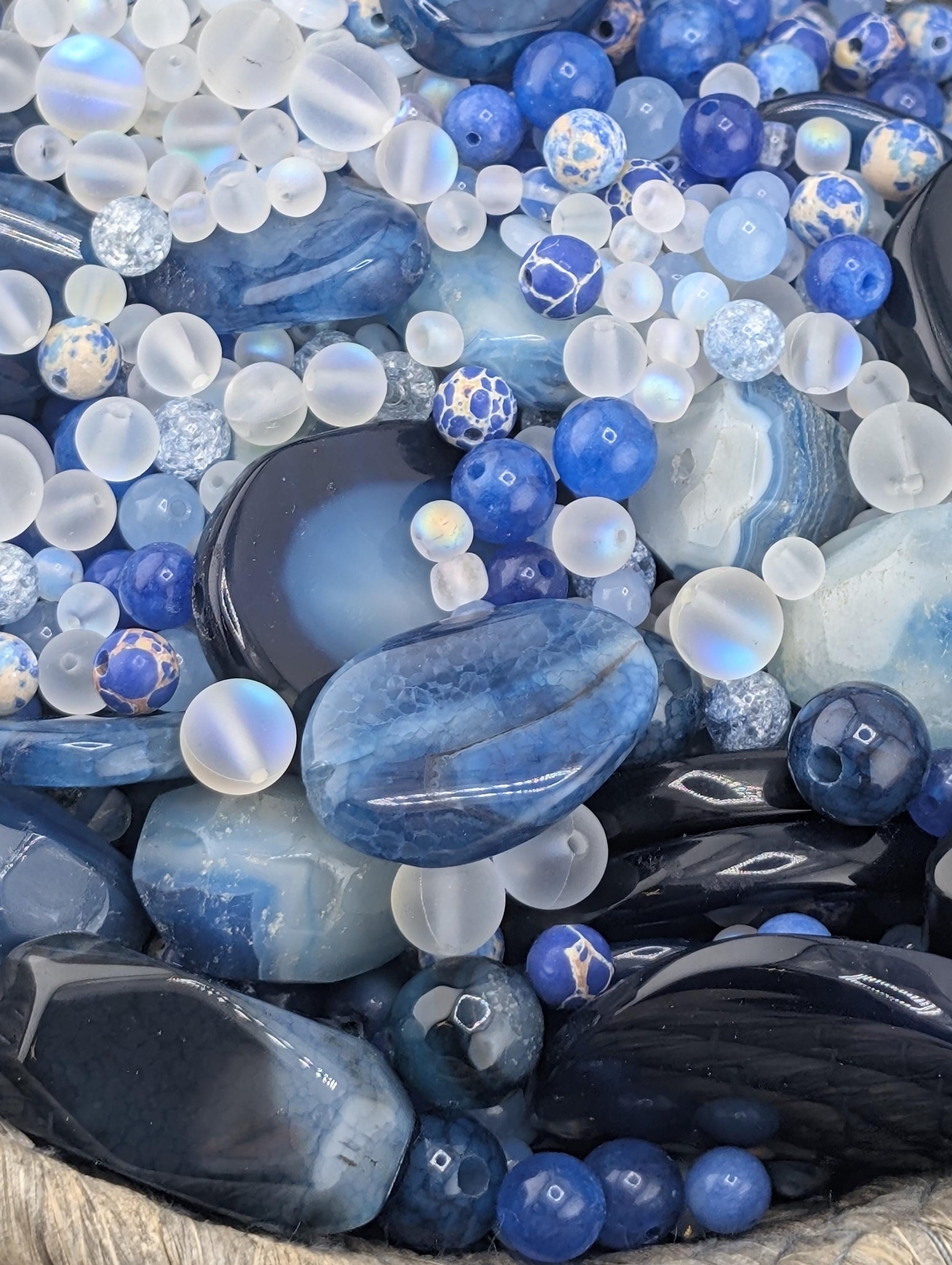 The image is a close-up of various blue and white gemstones and beads, including clear and blue stones, as well as some with a blue and white pattern.